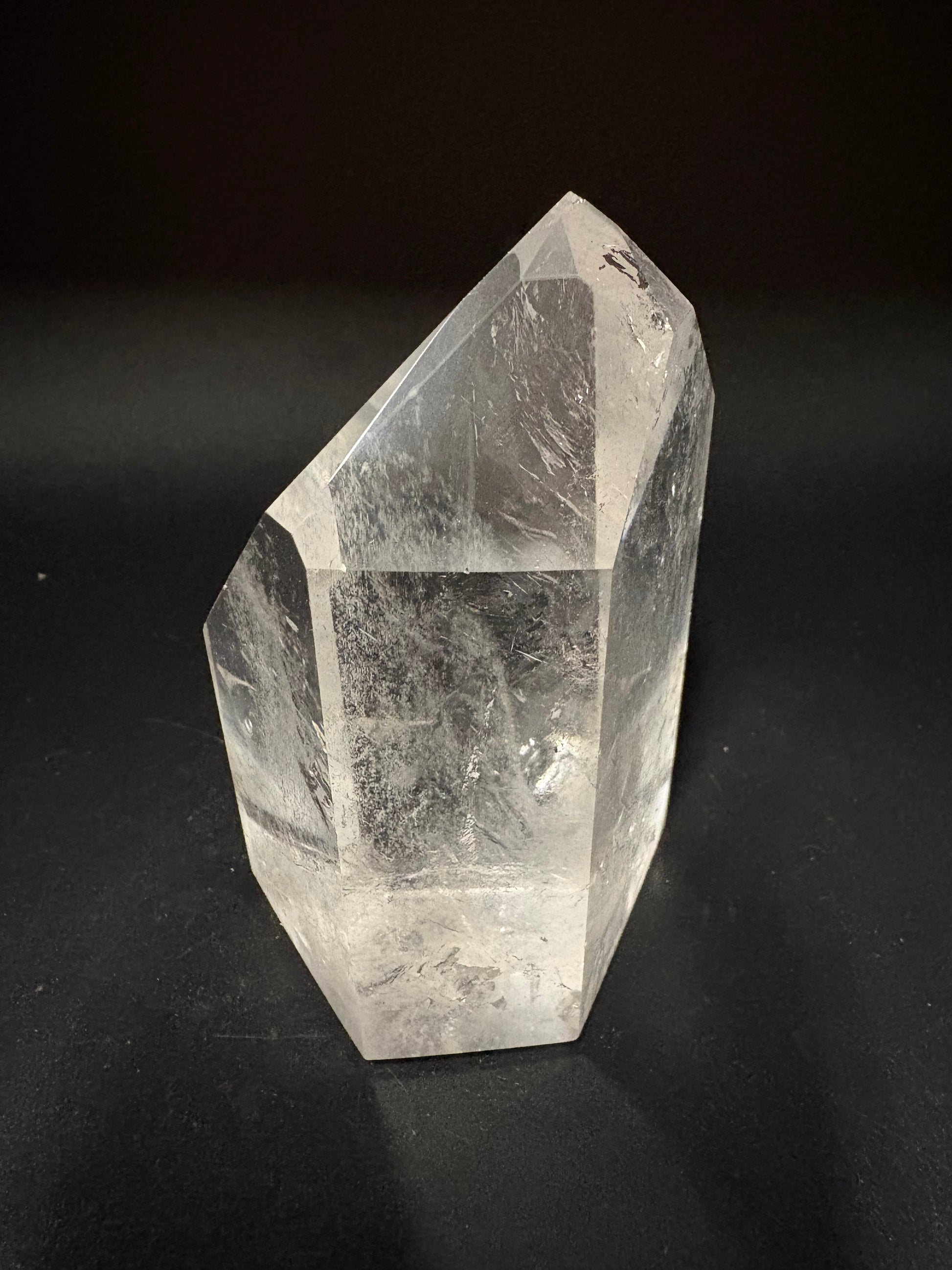 A clear quartz crystal point with visible internal inclusions, photographed on a dark black background.