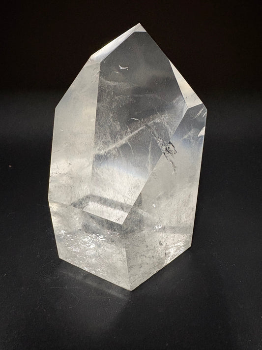 A faceted clear quartz crystal point with natural inclusions, displayed on a solid black background.