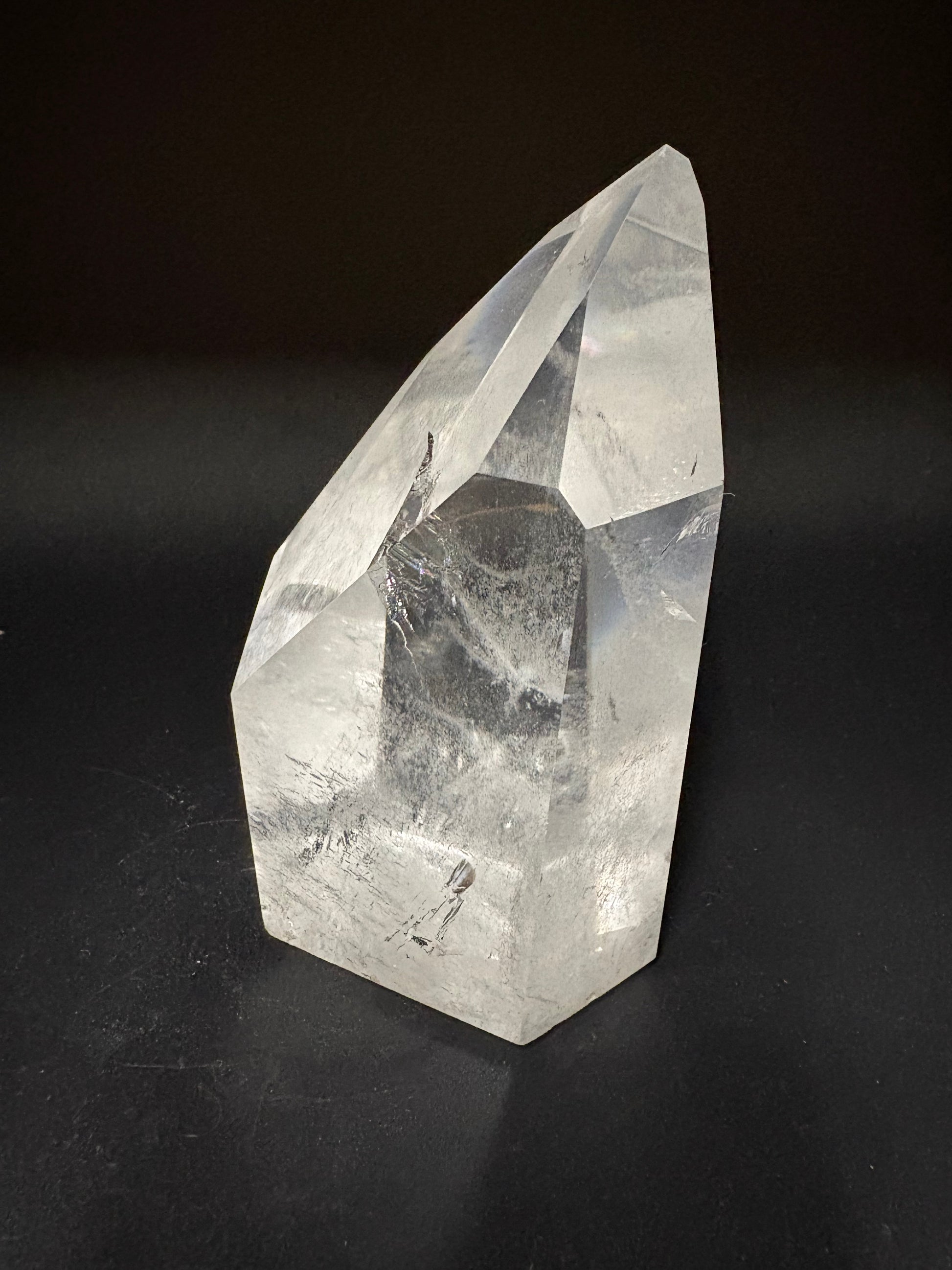 A faceted clear quartz crystal point with natural inclusions, displayed on a dark black background.