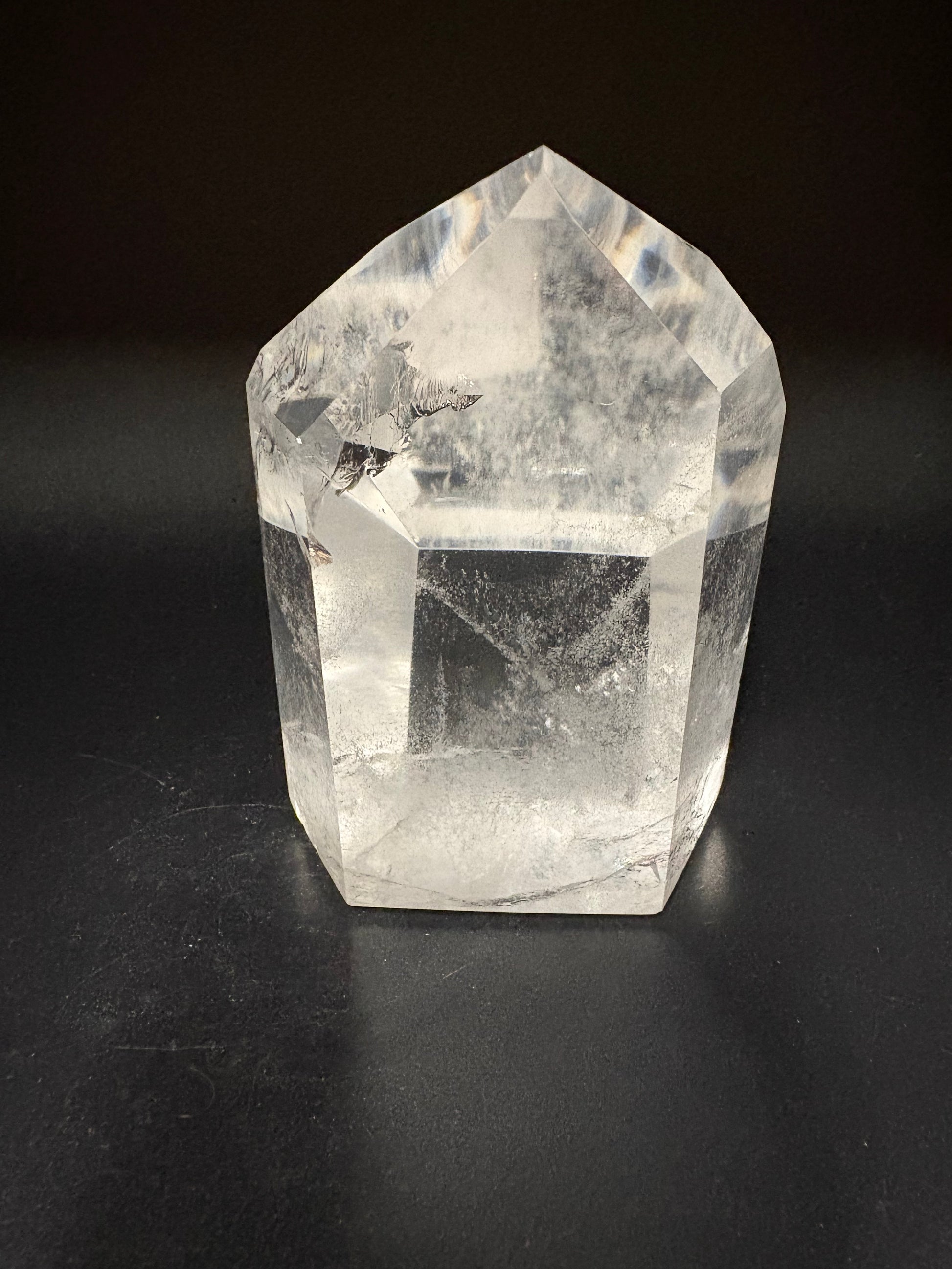A clear faceted crystal point, likely quartz, with natural inclusions, photographed on a dark black background.