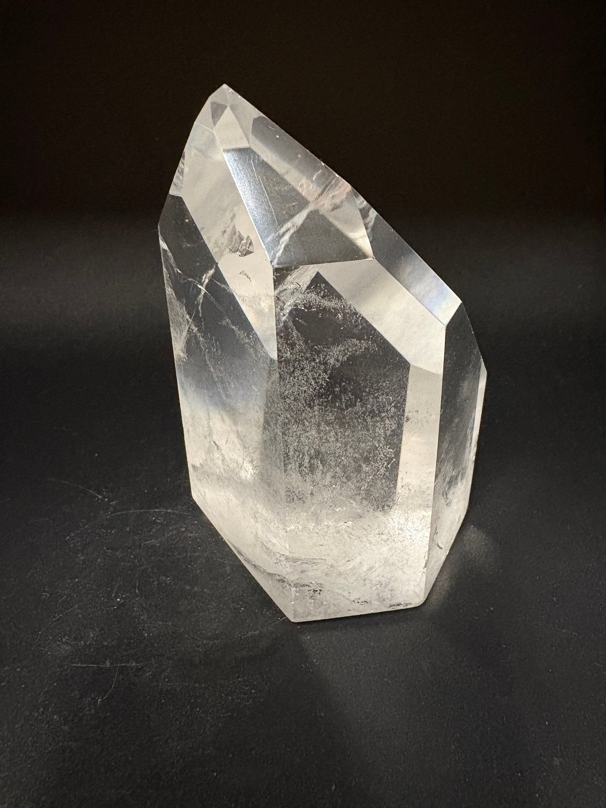 A faceted clear quartz crystal point with natural inclusions, displayed on a dark black background.