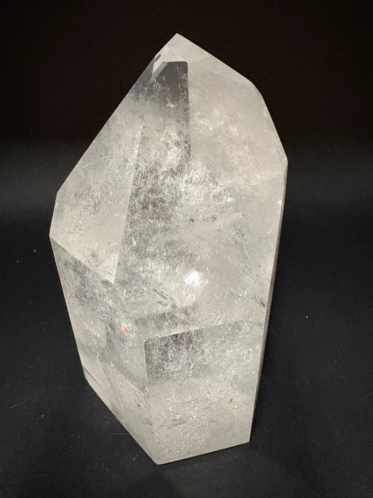 A raw, unpolished clear quartz crystal point with natural inclusions, displayed on a solid black background.