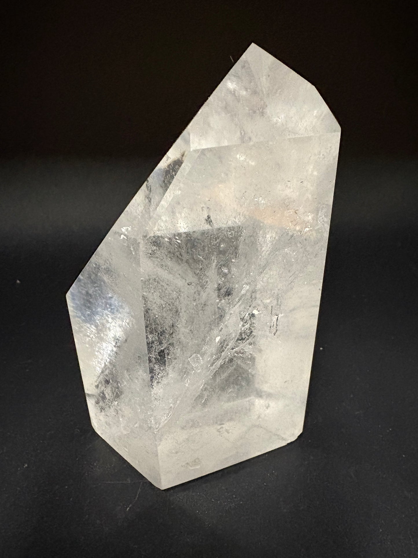 A natural clear quartz crystal point with internal inclusions, displayed on a dark black background.