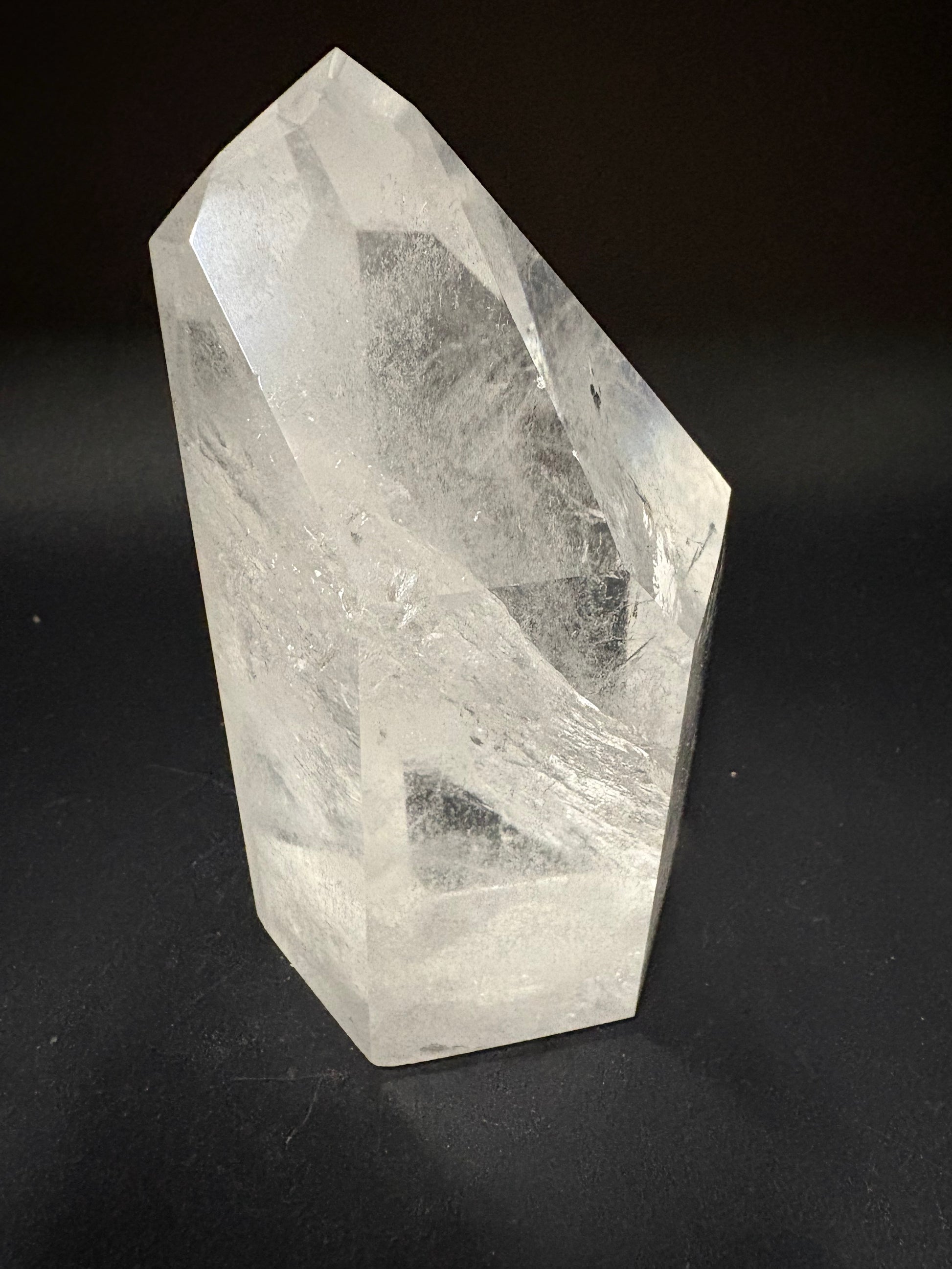 A faceted clear quartz crystal point with visible internal inclusions, photographed on a dark black background.