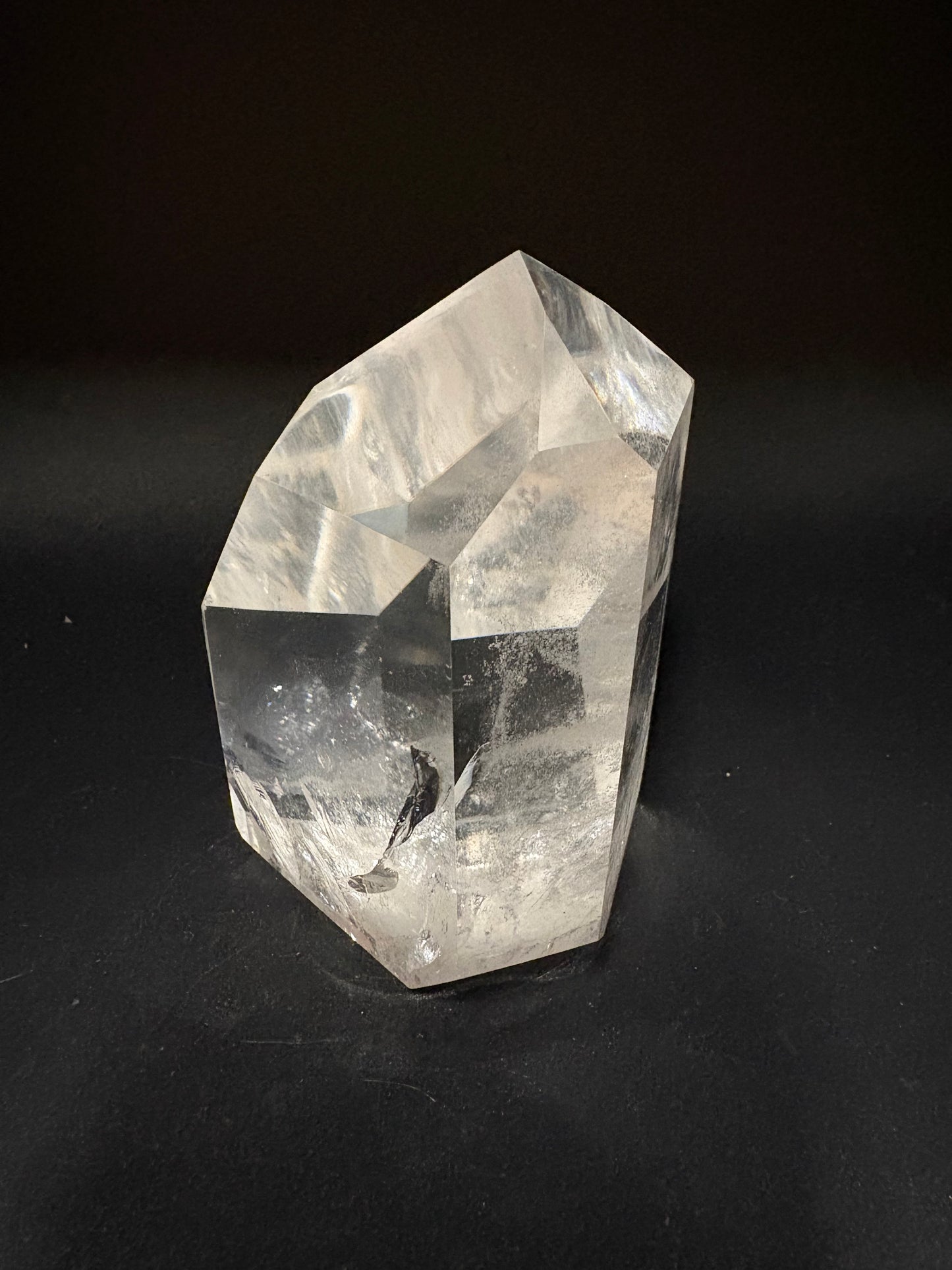 A raw, unpolished clear quartz crystal point with natural faceted edges and internal inclusions, photographed on a dark black background.