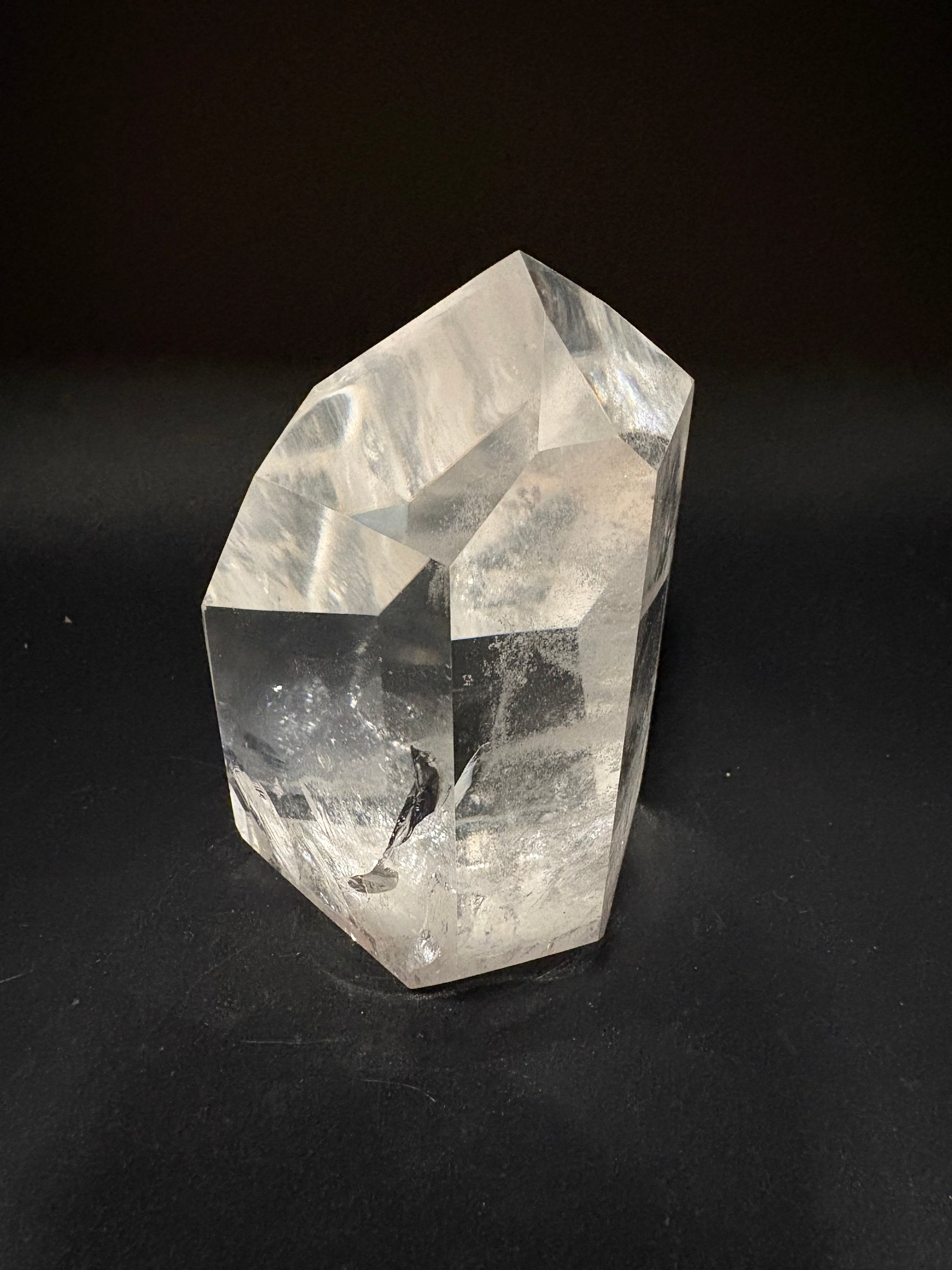 A raw, unpolished clear quartz crystal point with natural faceted edges and internal inclusions, photographed on a dark black background.