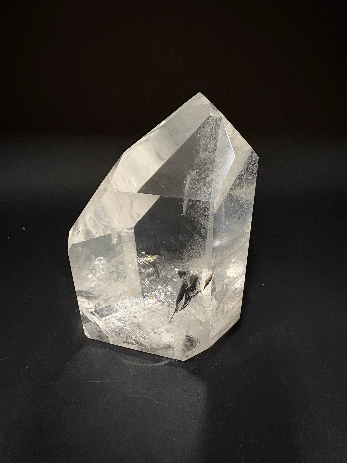 A clear quartz crystal point with natural inclusions, photographed on a dark black background.