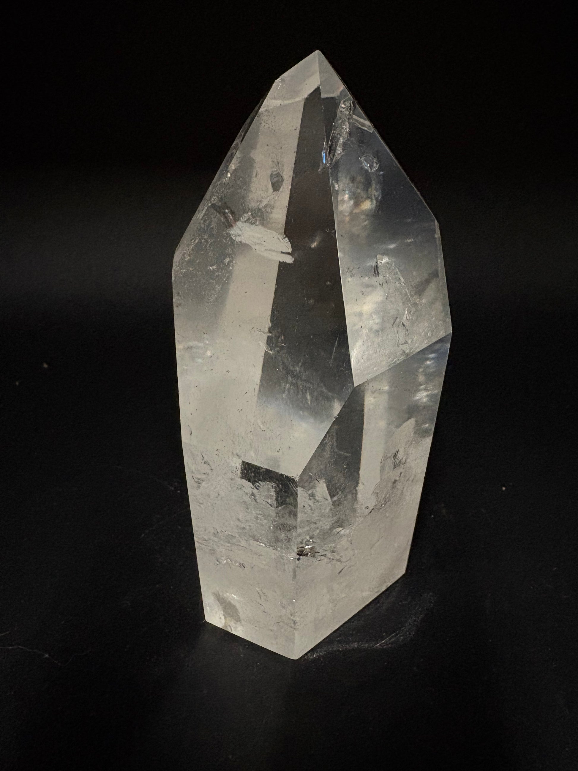 A clear faceted crystal point, likely quartz, photographed against a solid black background.