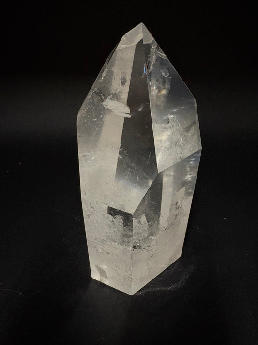 A clear faceted crystal point, likely quartz, photographed against a solid black background.