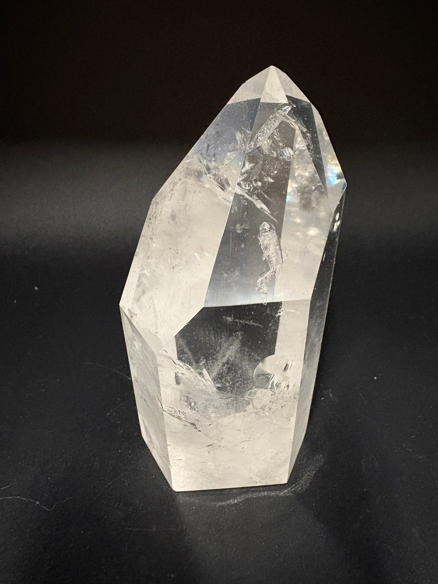 A natural clear quartz crystal point with faceted geometric edges, displayed on a dark black background.