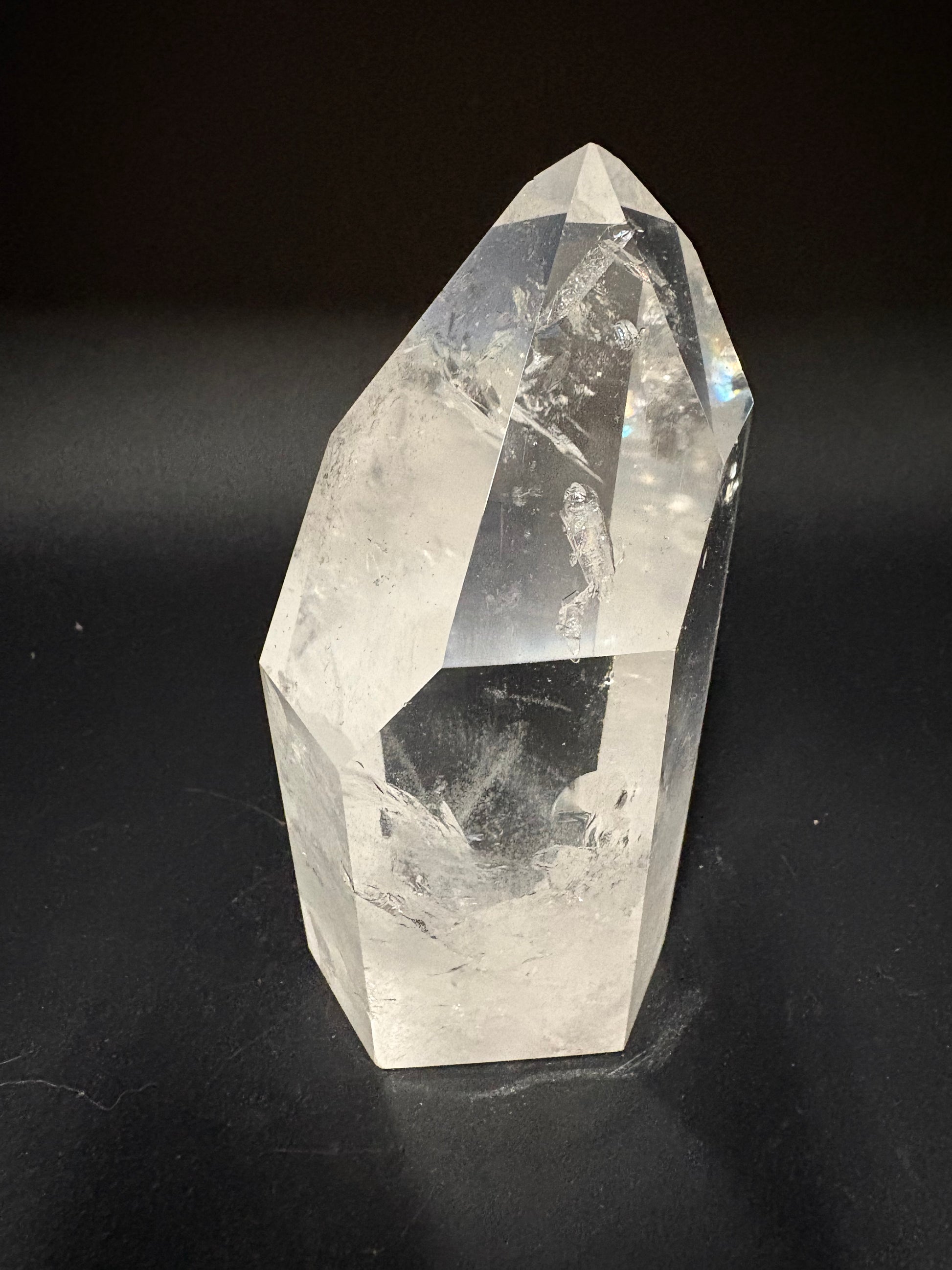 A natural clear quartz crystal point with faceted geometric edges, displayed on a dark black background.