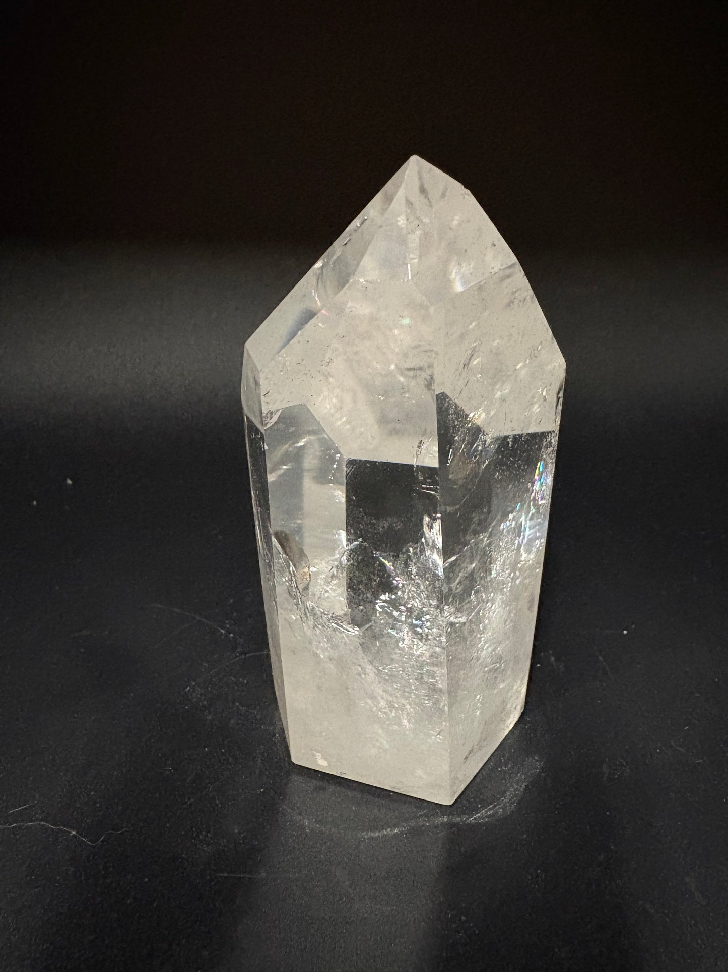 A clear quartz crystal point with natural inclusions, displayed on a dark black background.
