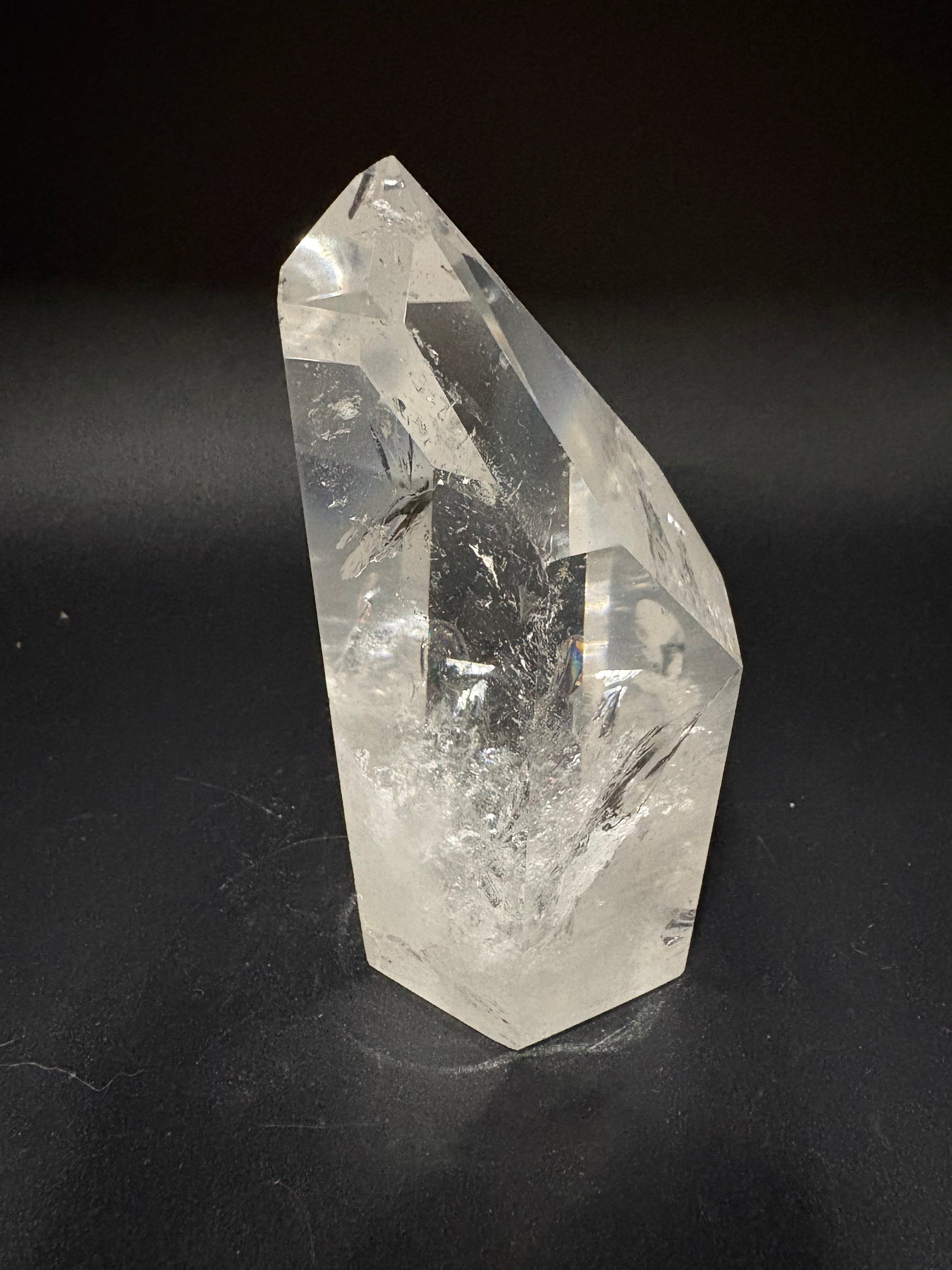 A clear faceted crystal point, likely quartz, resting on a dark black background.