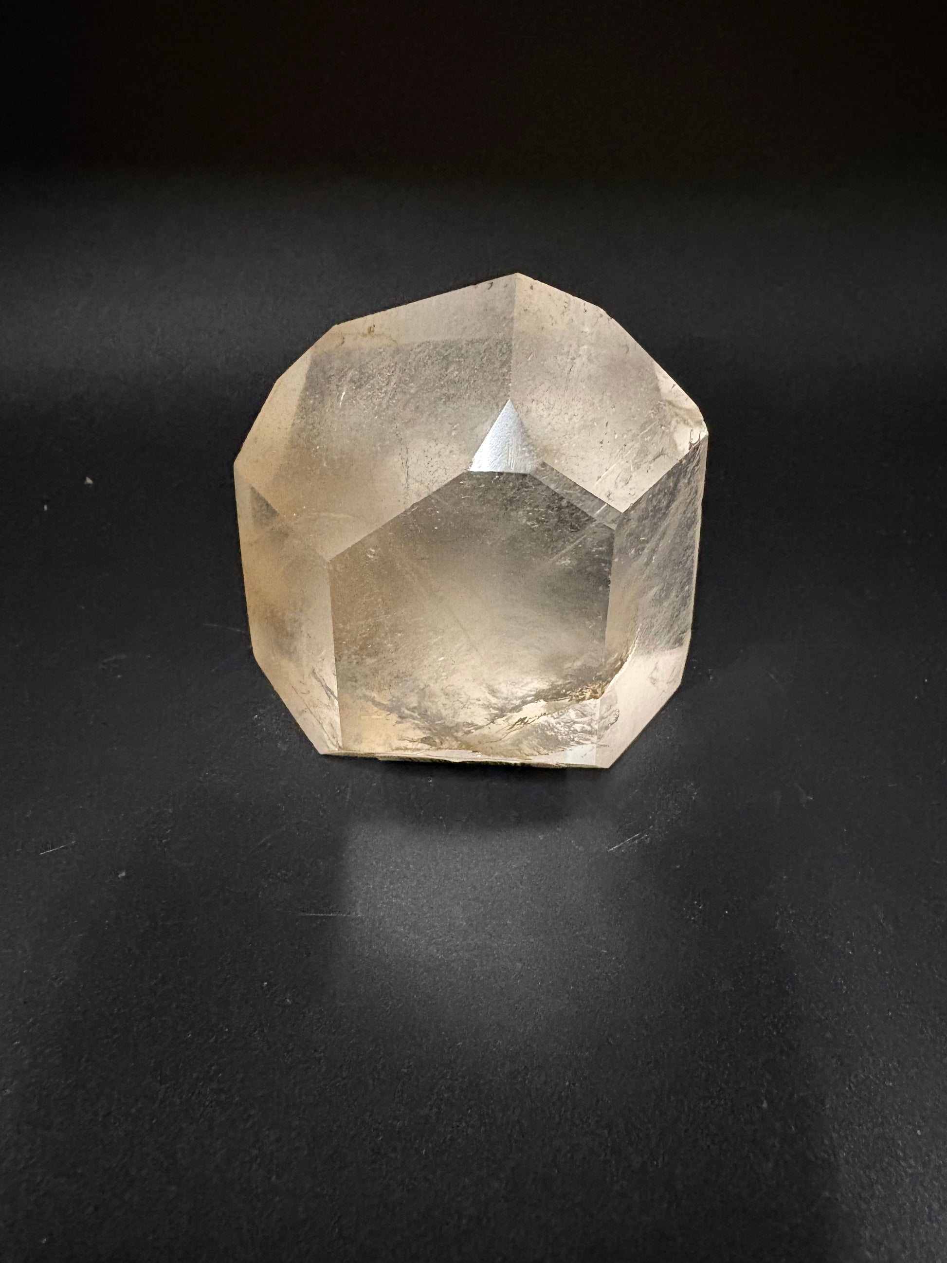 A faceted citrine crystal gemstone with natural inclusions, displayed on a dark black background.