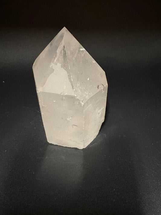 A raw, unpolished white quartz crystal point with natural faceted edges, resting on a dark black background.