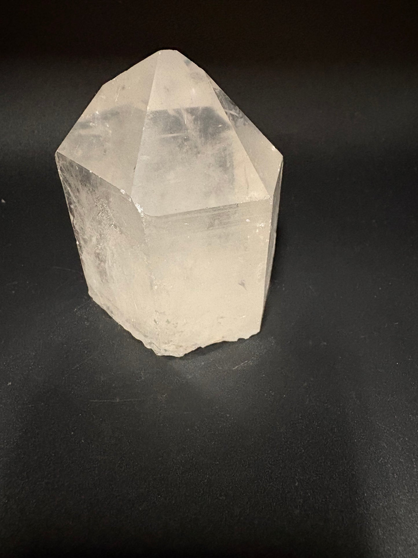 A raw, unpolished clear quartz crystal point with natural facets, resting on a dark black background.