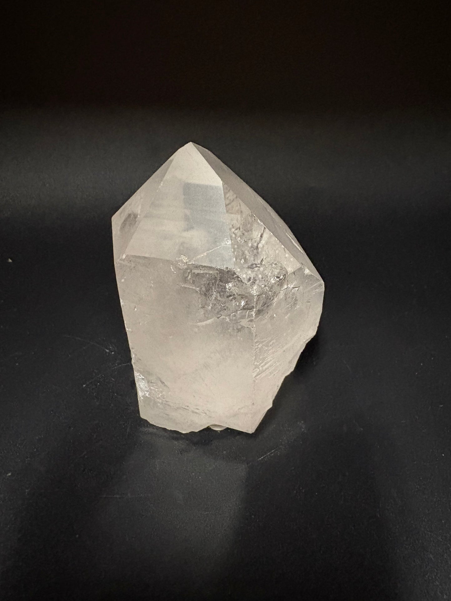 A raw, unpolished clear quartz crystal point with natural facets, resting on a dark black background.