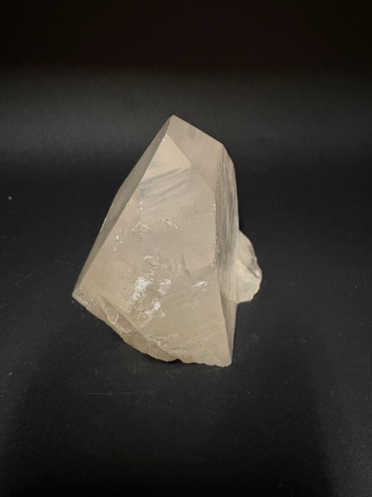 A raw, faceted crystal stone with a rough, natural top edge, shown on a dark, solid background.