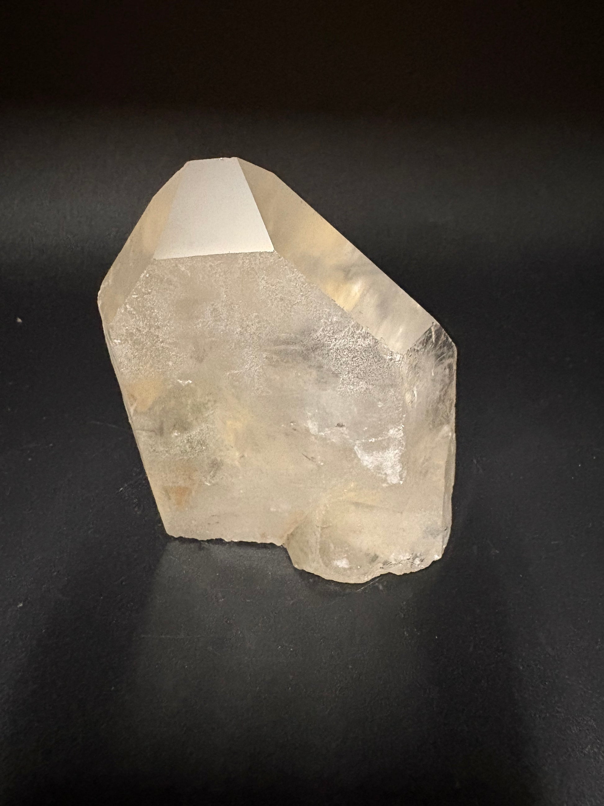 A rough, unpolished natural quartz crystal with a prominent pointed tip, showing a translucent off-white color, set against a dark black background.