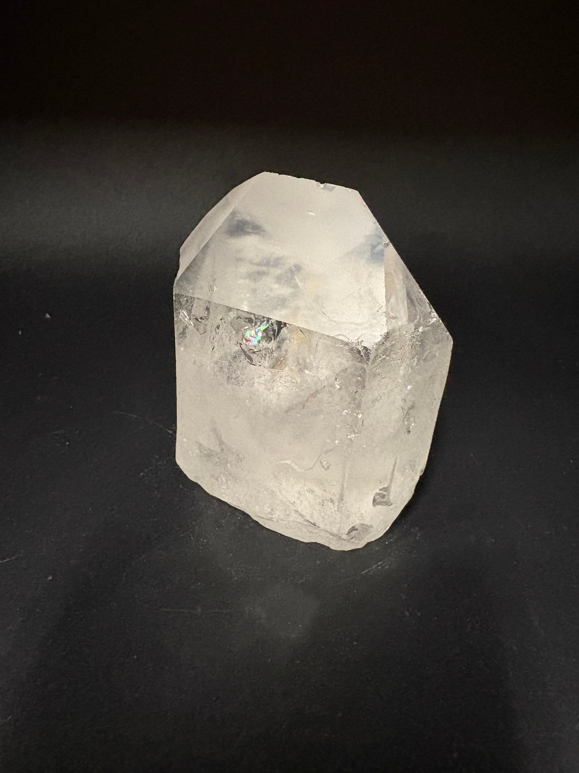 A raw, unpolished clear quartz crystal with natural facets and inclusions, resting on a dark black background.