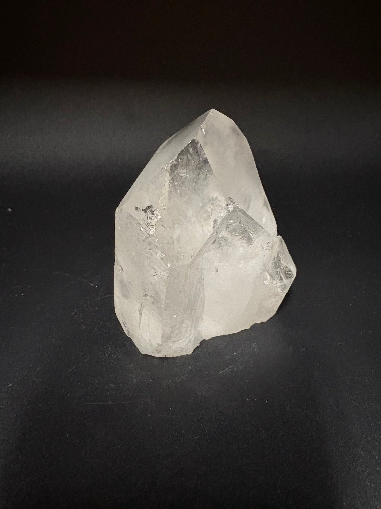 A rough, uncut clear quartz crystal with natural geometric facets, displayed on a dark, solid background.