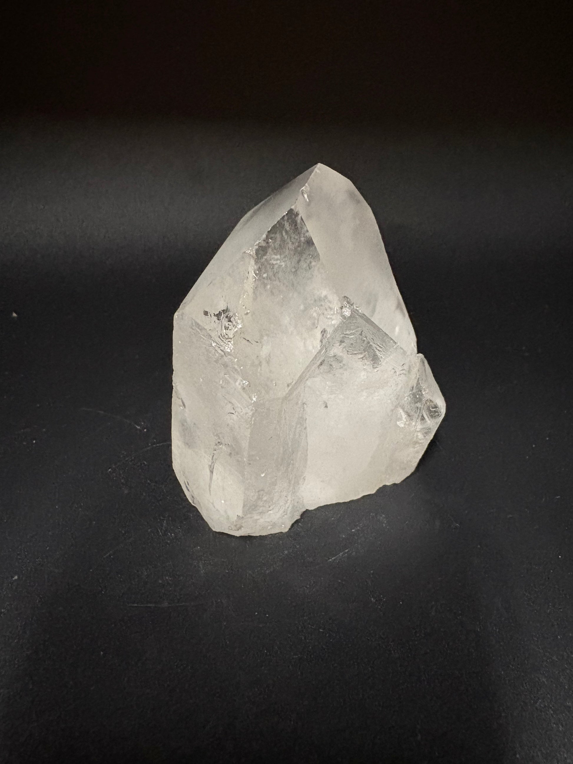 A rough, uncut clear quartz crystal with natural geometric facets, displayed on a dark, solid background.