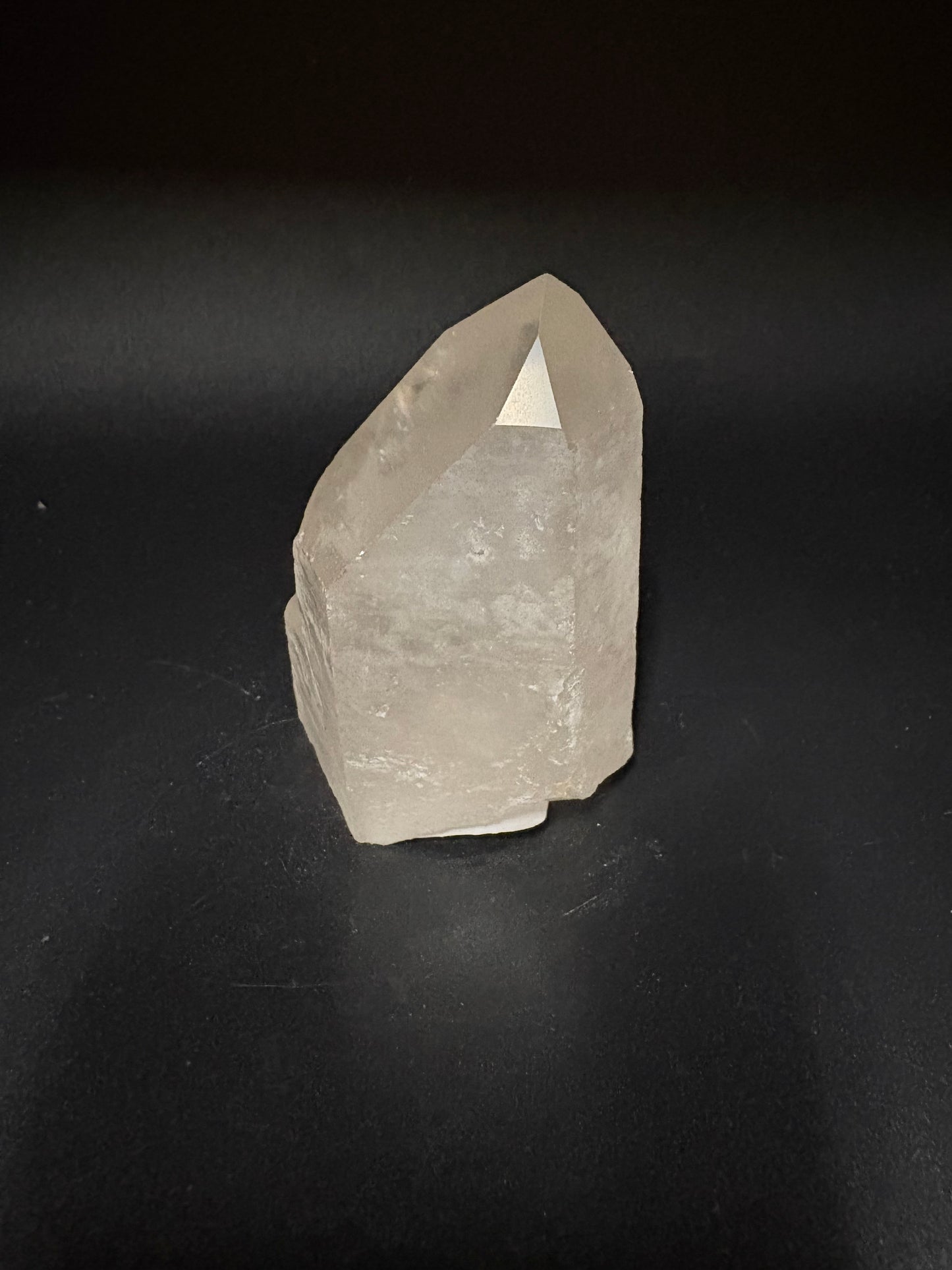 A raw, unpolished quartz crystal with a pointed tip, resting on a dark black surface.