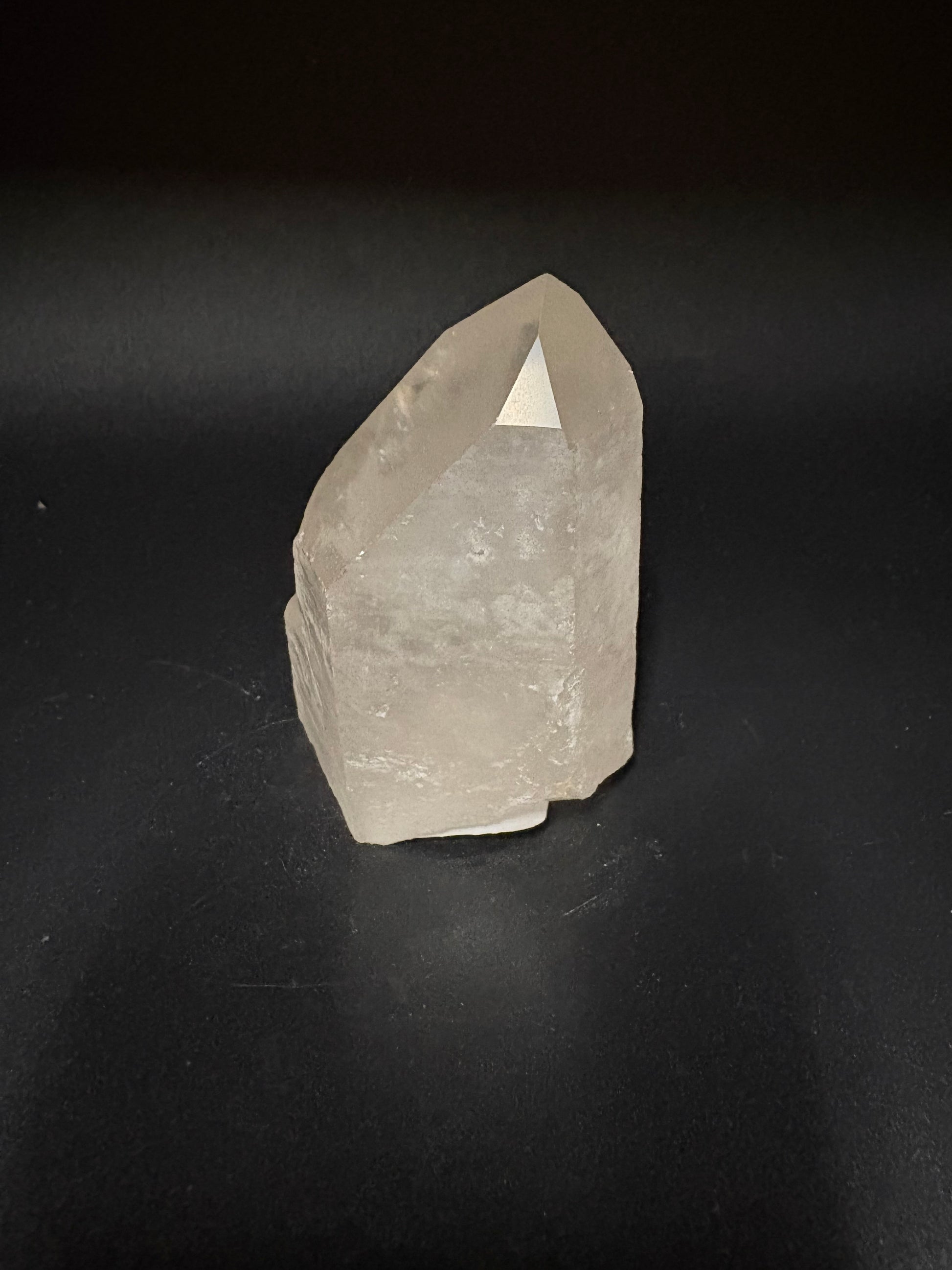 A raw, unpolished quartz crystal with a pointed tip, resting on a dark black surface.