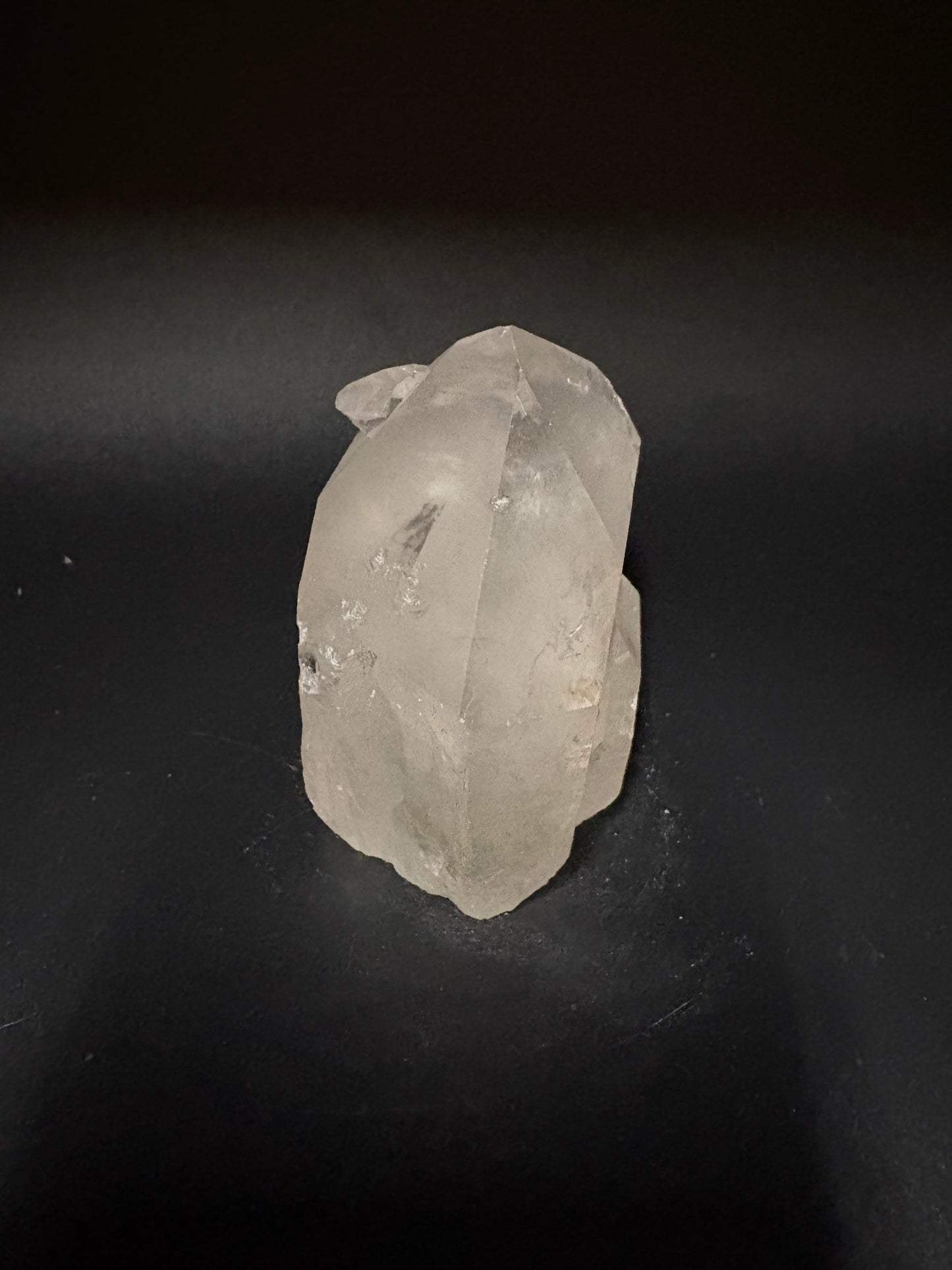 A raw, unpolished translucent crystal stone with natural facets, resting on a dark black background.