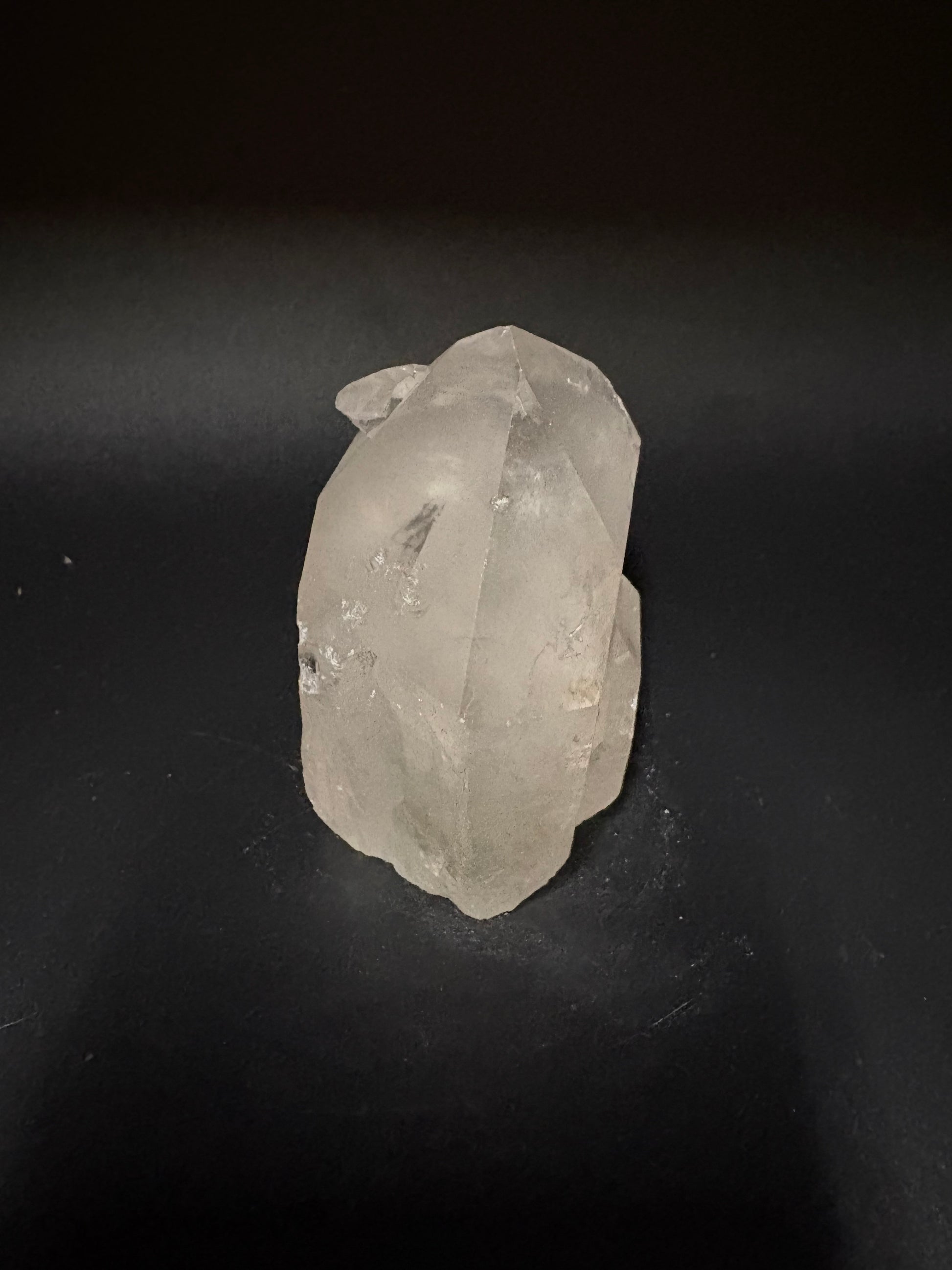 A raw, unpolished translucent crystal stone with natural facets, resting on a dark black background.