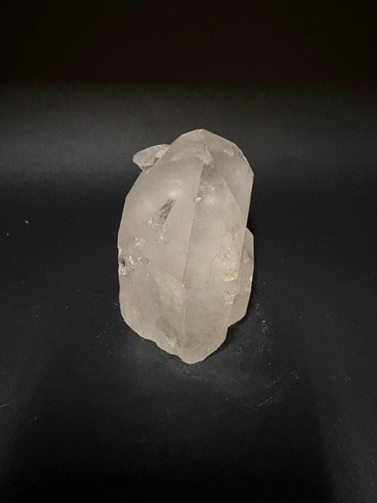 A raw, unpolished translucent crystal stone with natural facets, resting on a dark black background.
