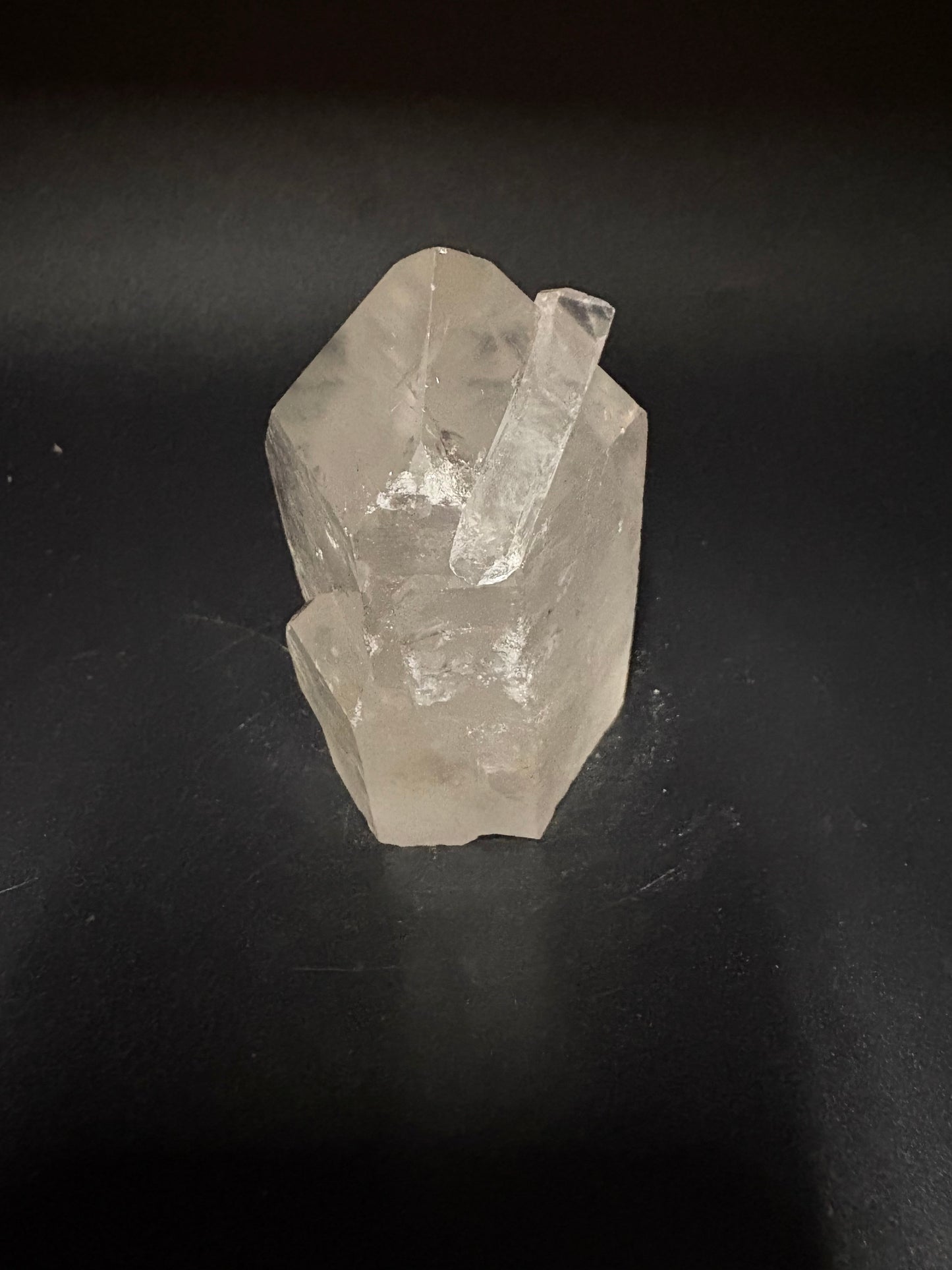 A rough, unpolished clear quartz crystal with natural facets, resting on a dark, matte surface.