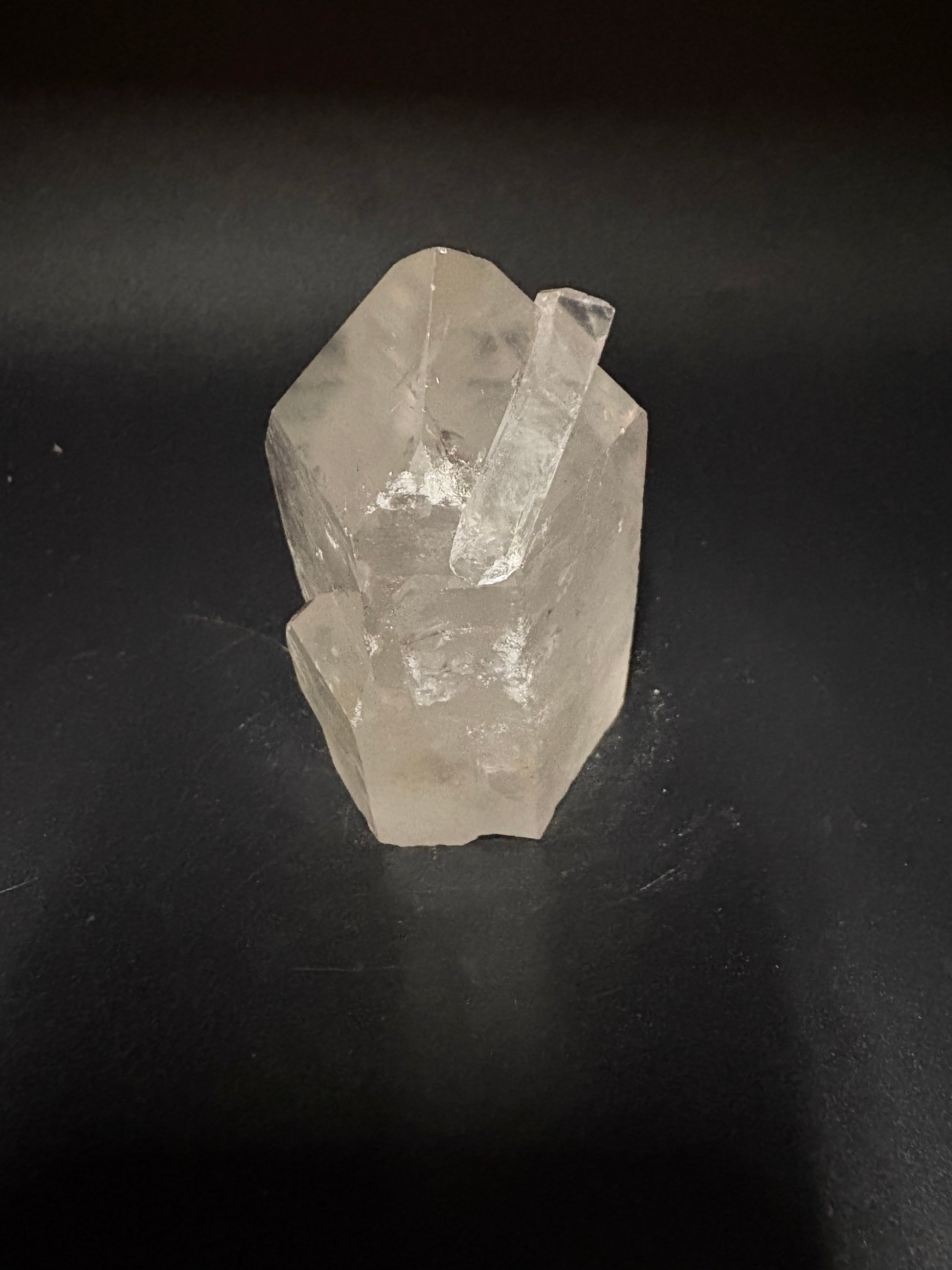 A rough, unpolished clear quartz crystal with natural facets, resting on a dark, matte surface.