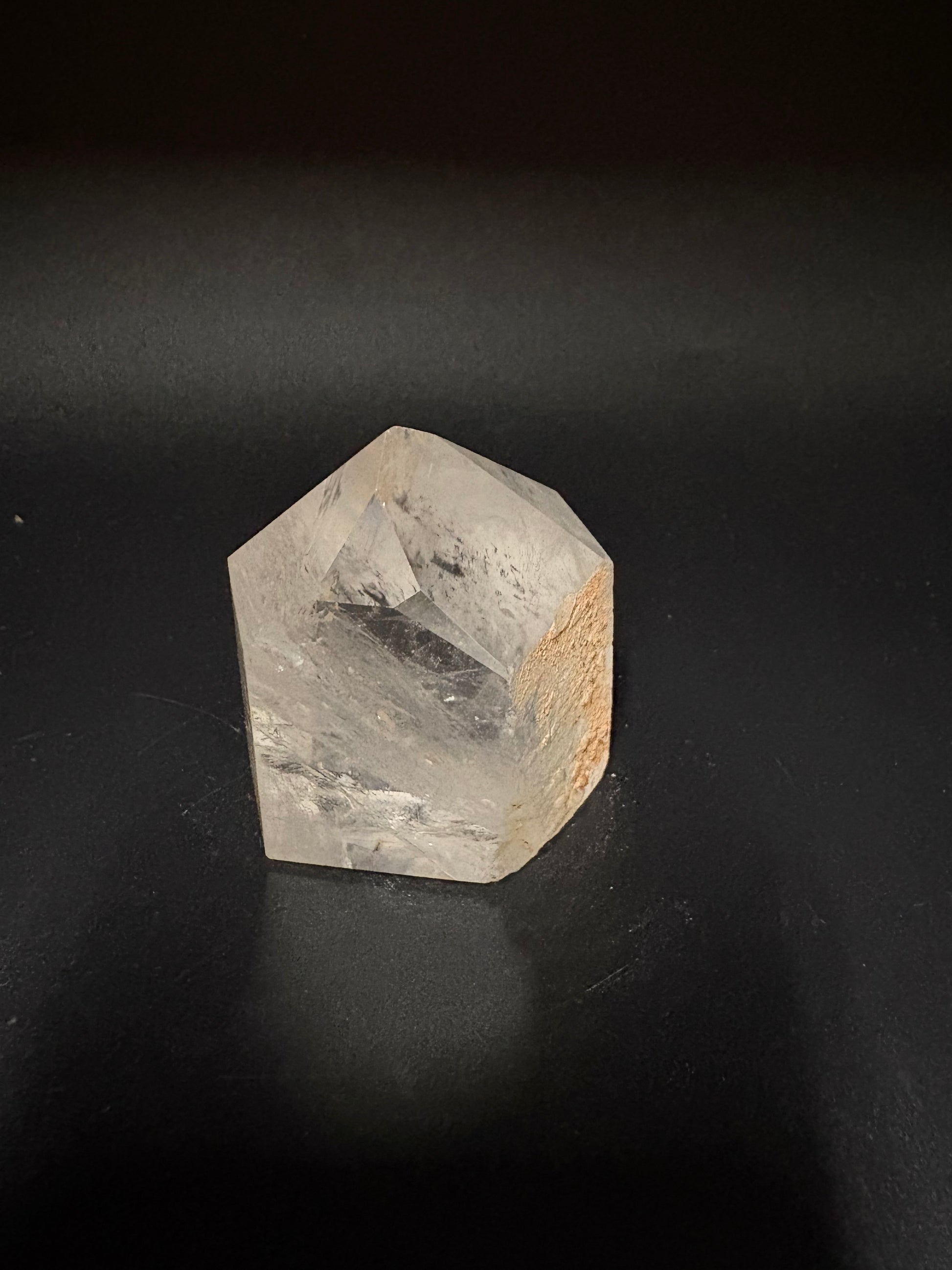 A raw, unpolished clear quartz crystal with a natural rough texture and a light brown matrix, shown on a dark black background.