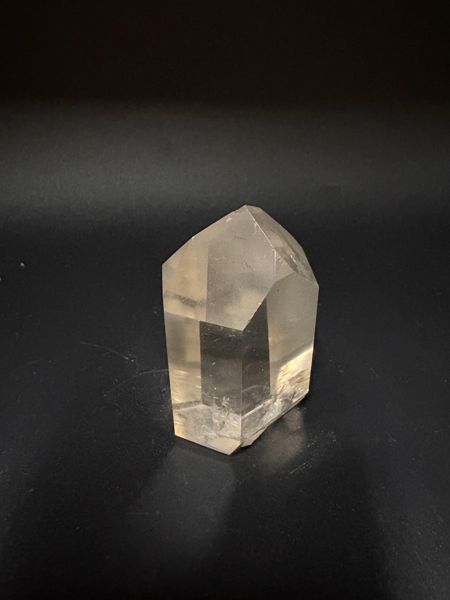 A faceted clear quartz crystal point resting on a dark, matte background.
