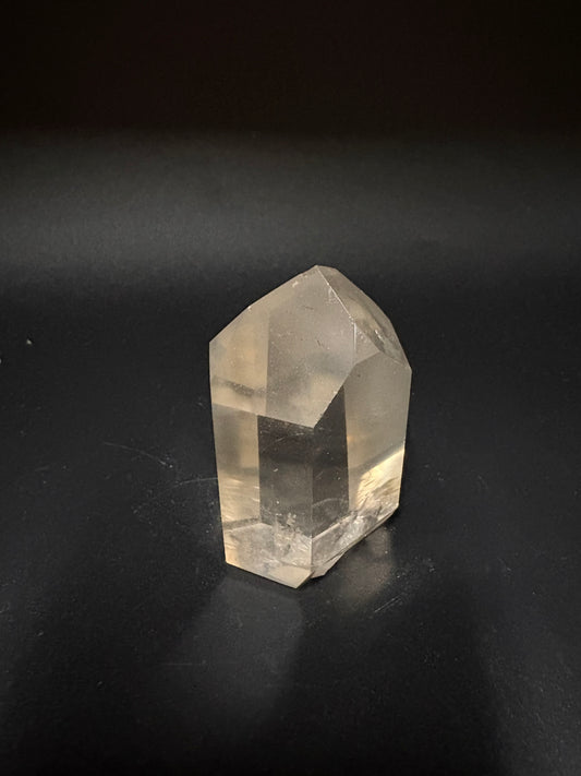A faceted clear quartz crystal point resting on a dark, matte background.