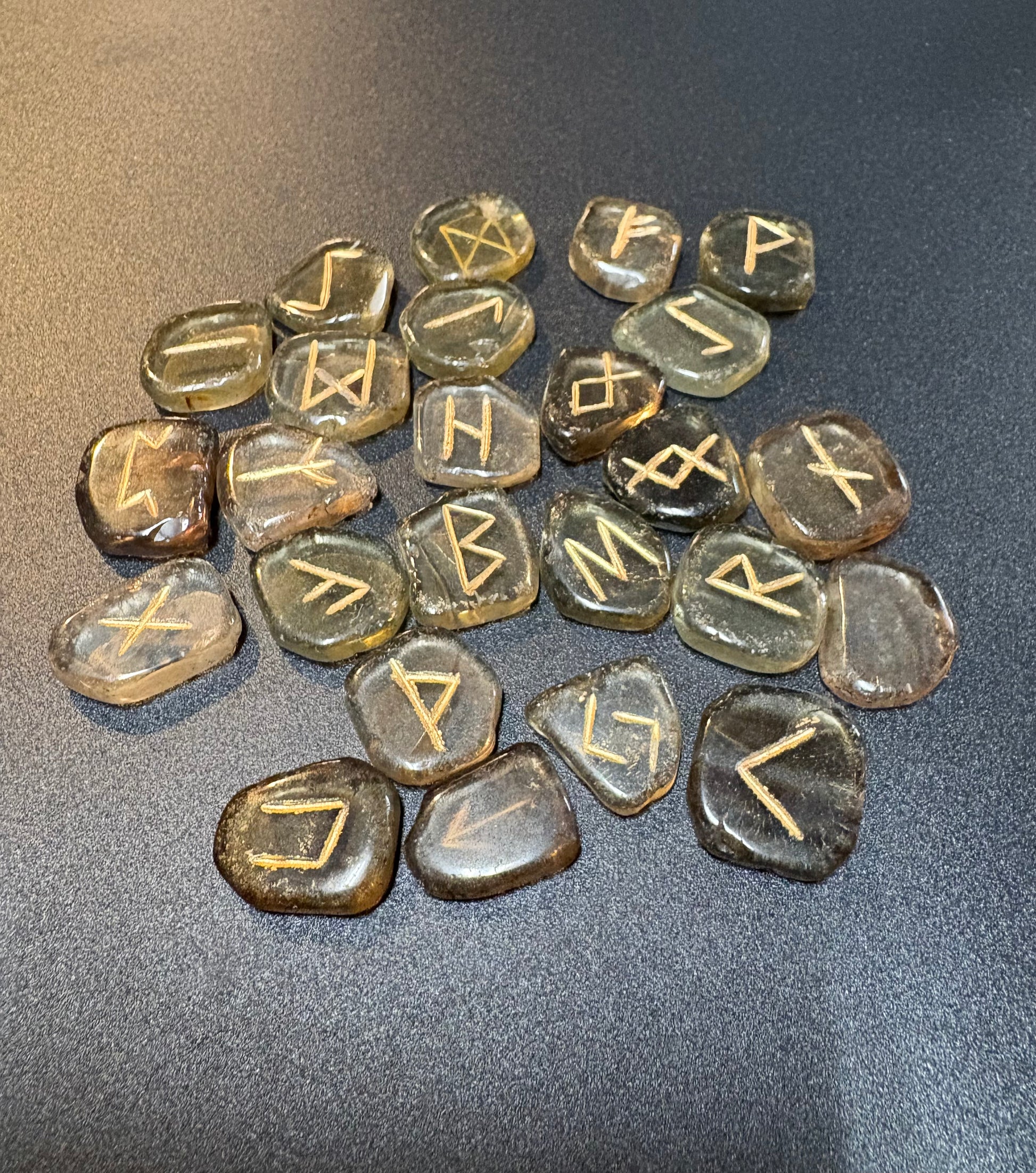 A group of polished smoky quartz stones engraved with runic symbols, arranged on a dark gray textured surface.