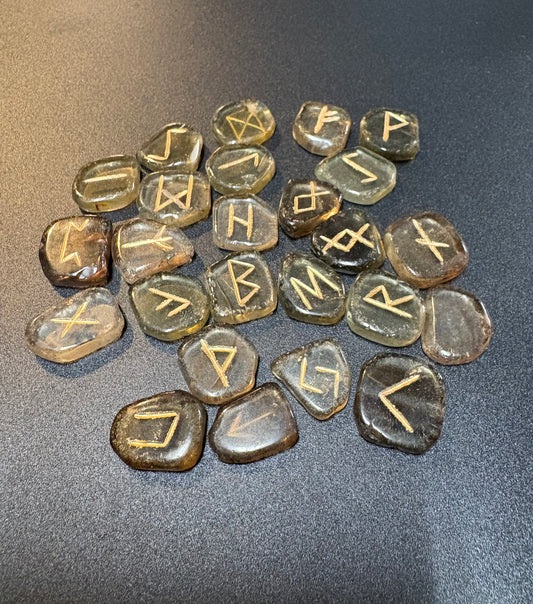A group of polished smoky quartz stones engraved with runic symbols, arranged on a dark gray textured surface.