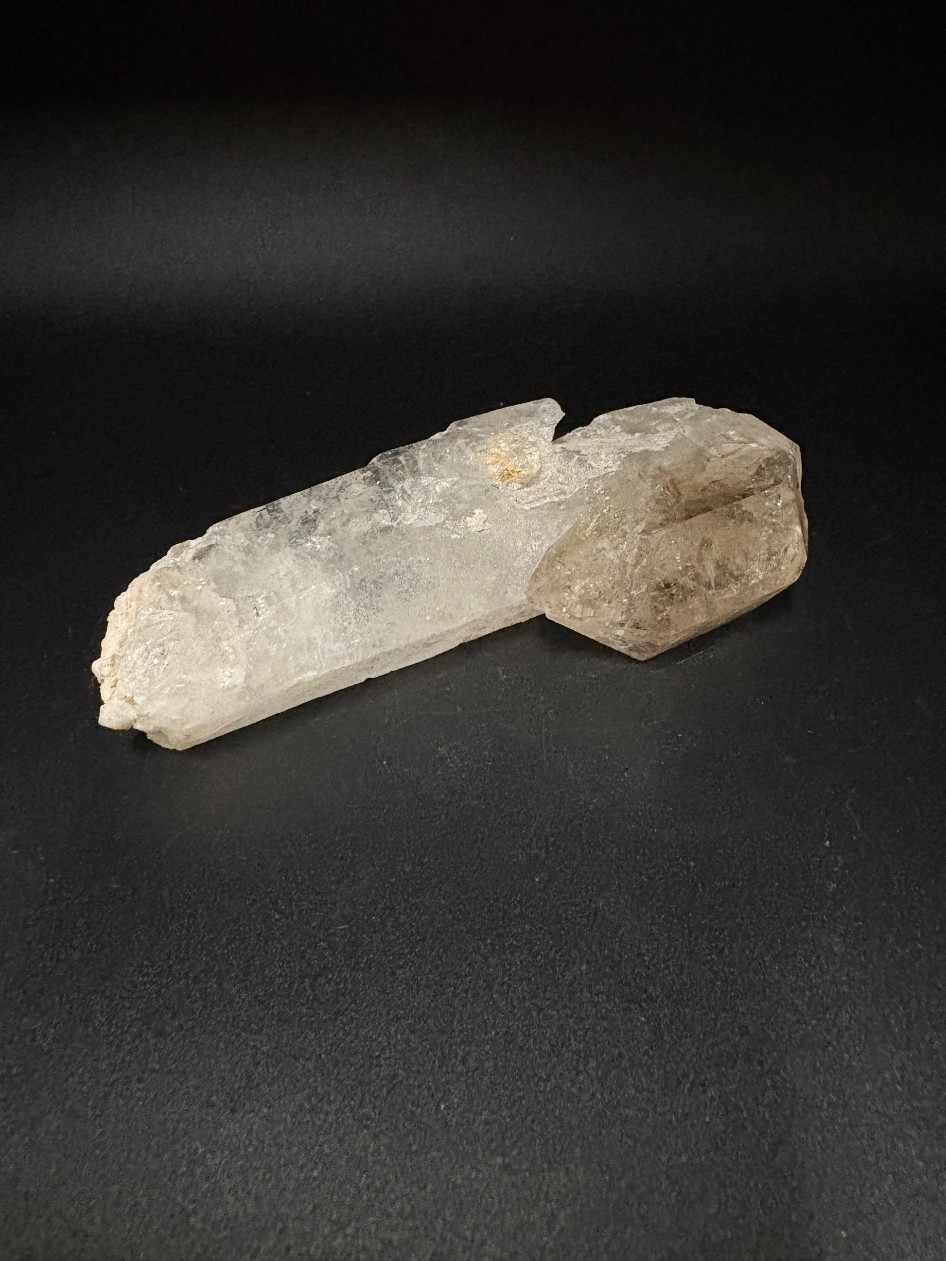 A raw dual-toned crystal cluster, featuring a prominent translucent pale gray point on the left and a denser, smoky brownish-gray section on the right, resting on a dark black background.