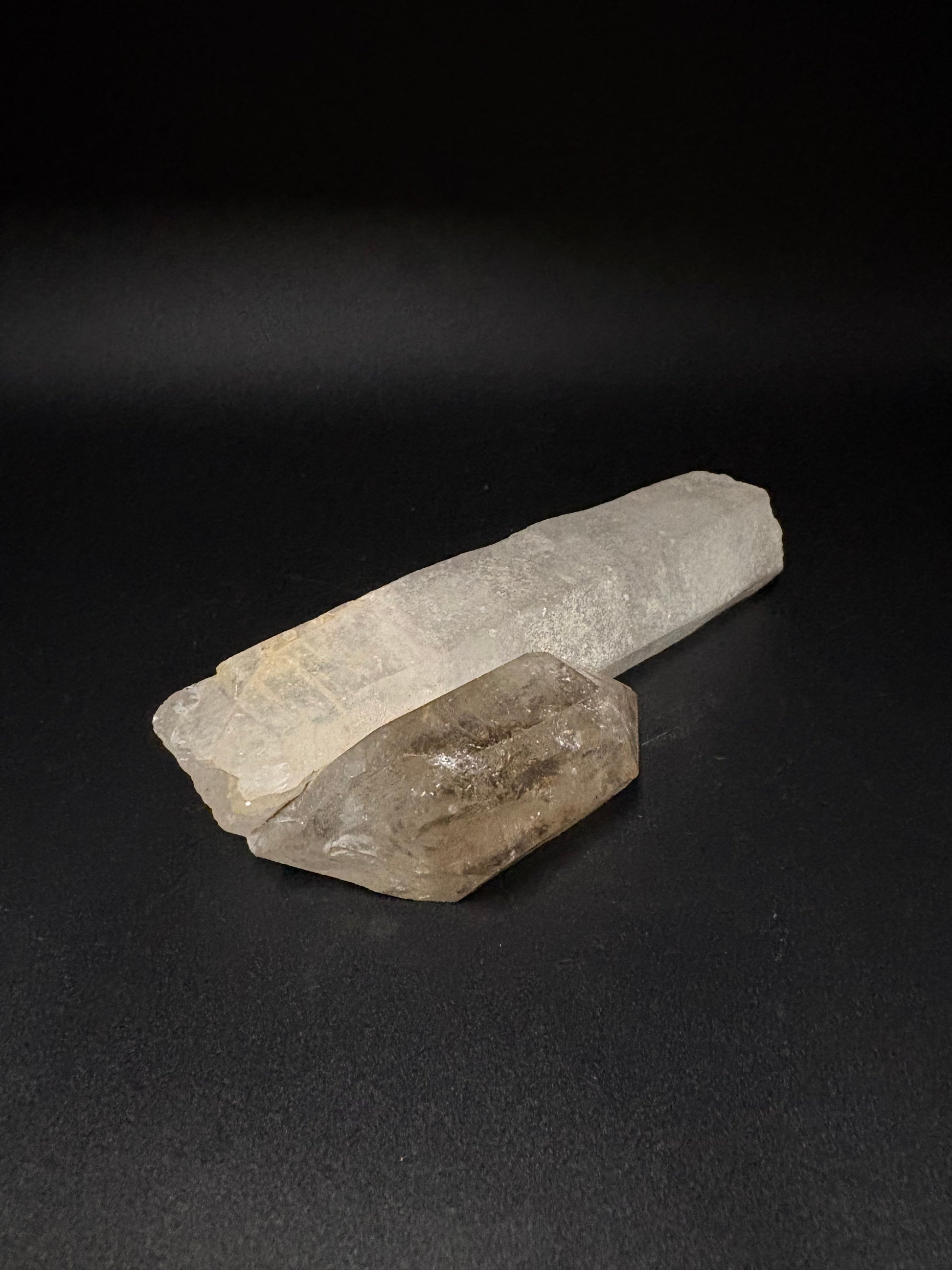 Two raw crystal points, one pale milky white and one smoky translucent brown, displayed on a dark black background.