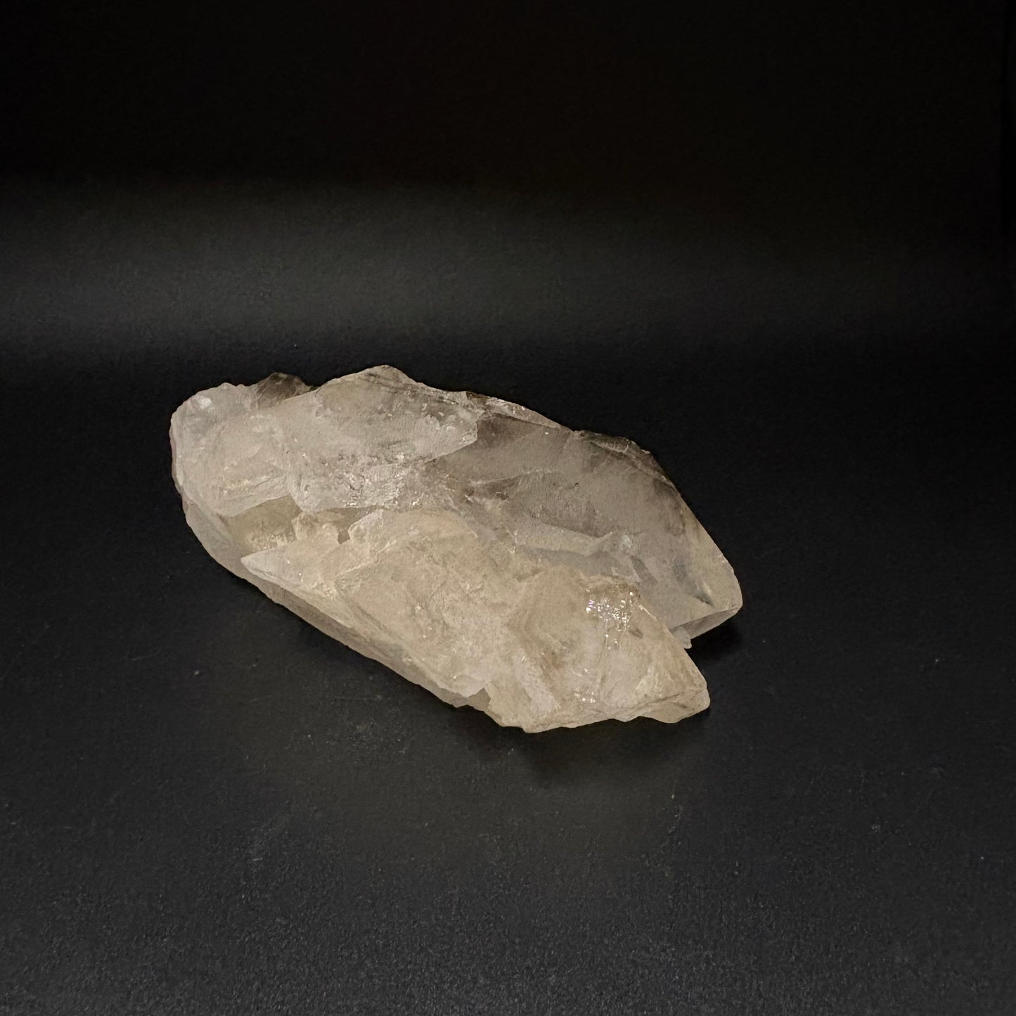 A raw, rough crystal cluster of translucent pale quartz with natural jagged edges, displayed on a dark black background.