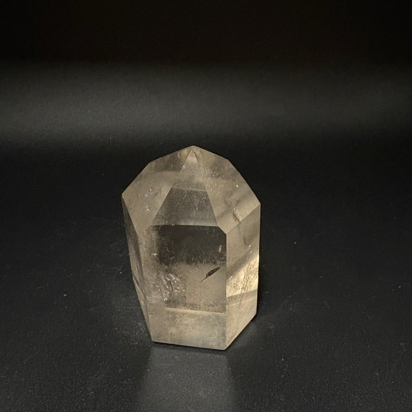 A natural clear quartz crystal point with geometric facets, photographed on a dark black background.