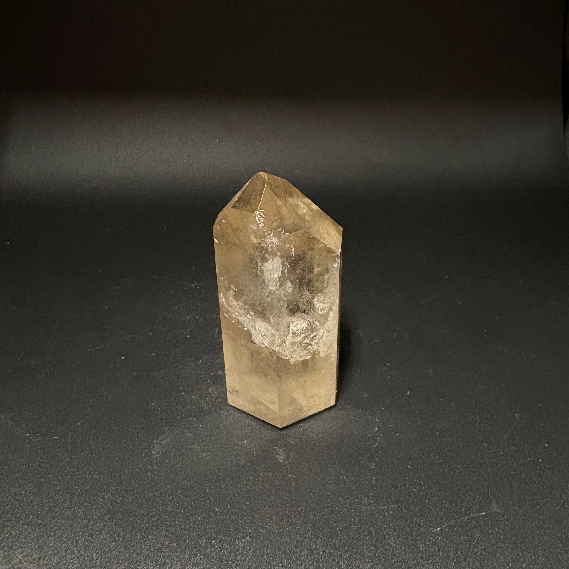 A natural clear quartz crystal point with internal inclusions, standing upright on a dark gray surface against a dark background.