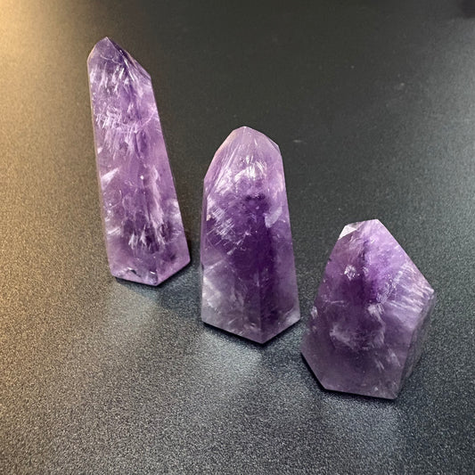 Three natural amethyst crystal points of different heights arranged on a dark gray textured surface.
