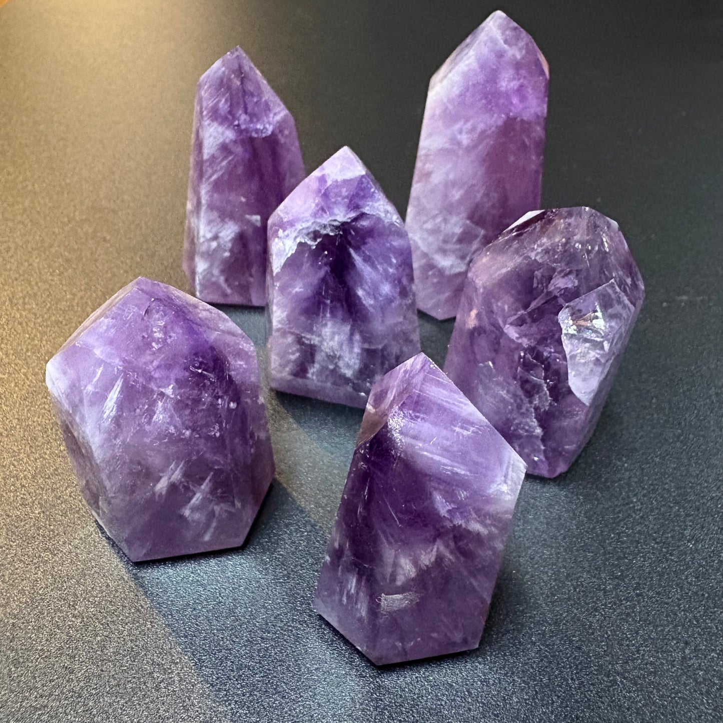 Six polished purple amethyst crystal points arranged on a dark gray surface.