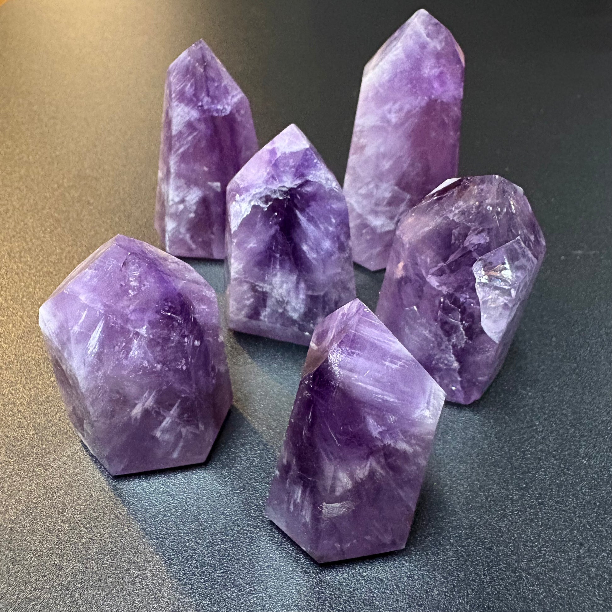 Six polished purple amethyst crystal points arranged on a dark gray surface.