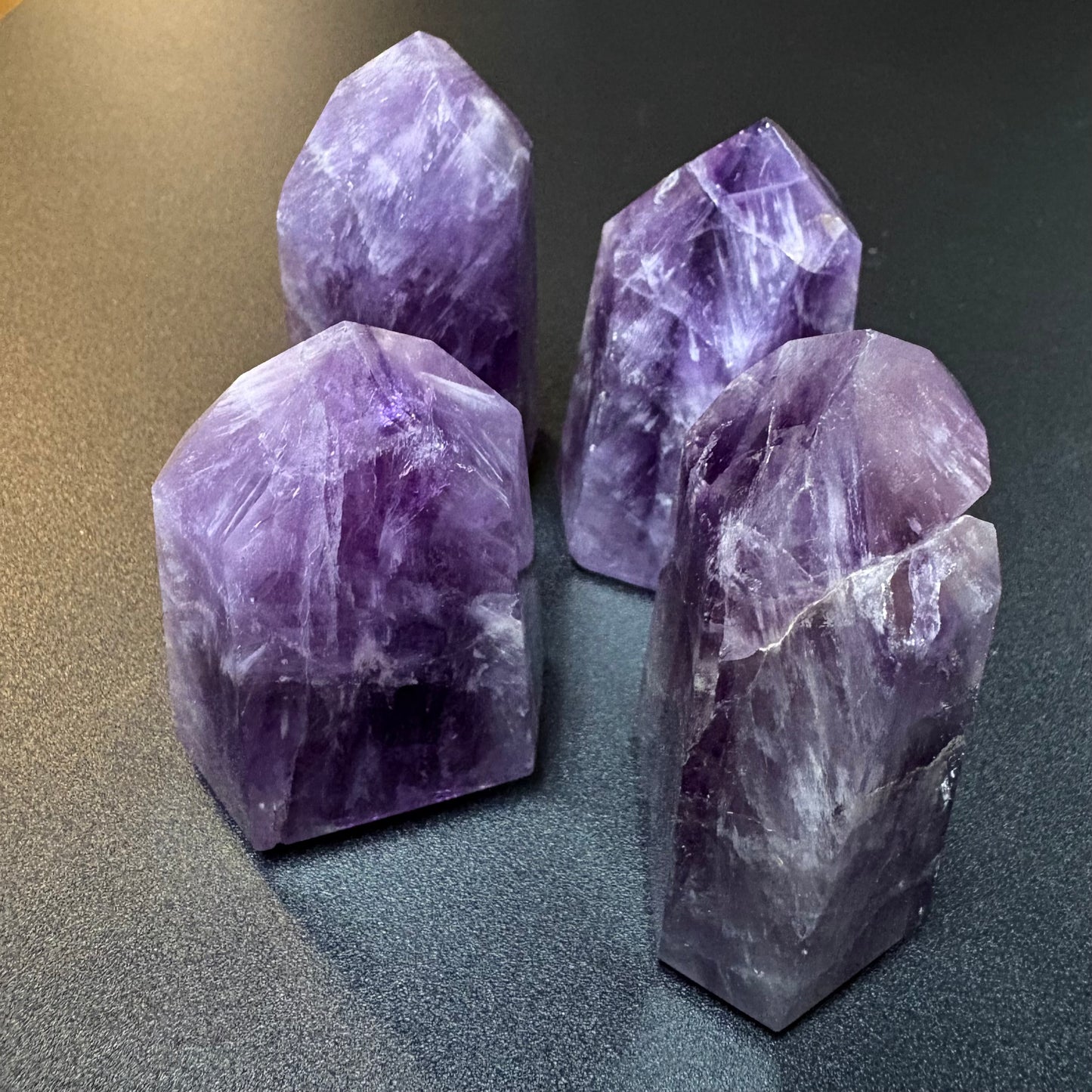 Four polished purple amethyst crystal towers of varying heights arranged on a dark gray textured surface.