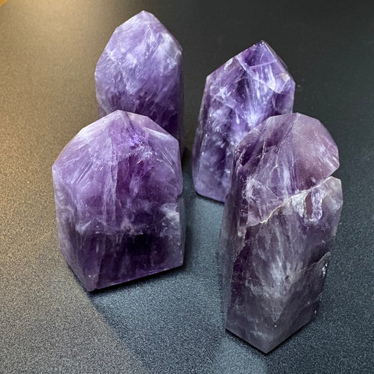 Four polished purple amethyst crystal towers of varying heights arranged on a dark gray textured surface.