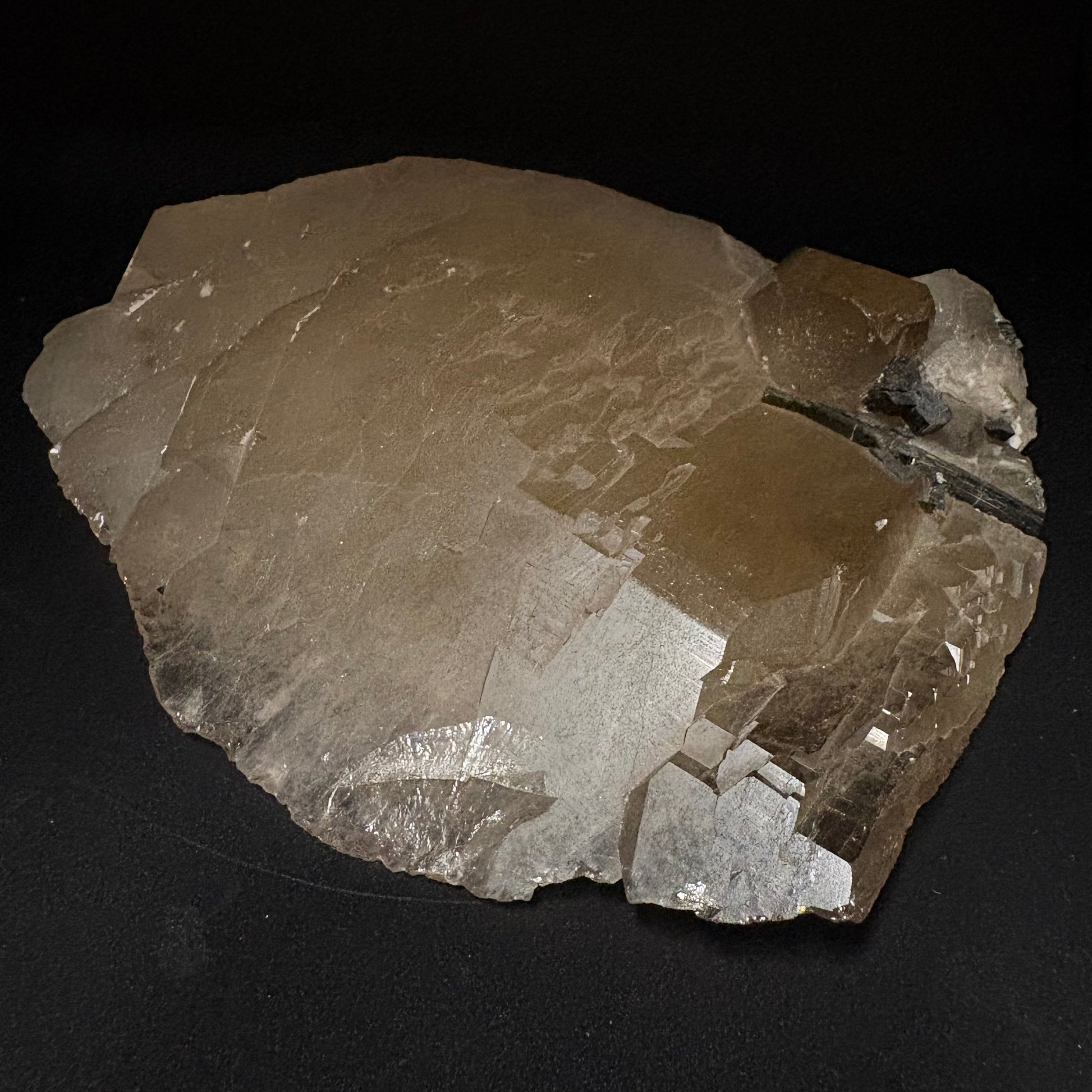 A raw quartz crystal cluster specimen with natural rough edges and a prominent cleavage plane, displayed on a solid black background.