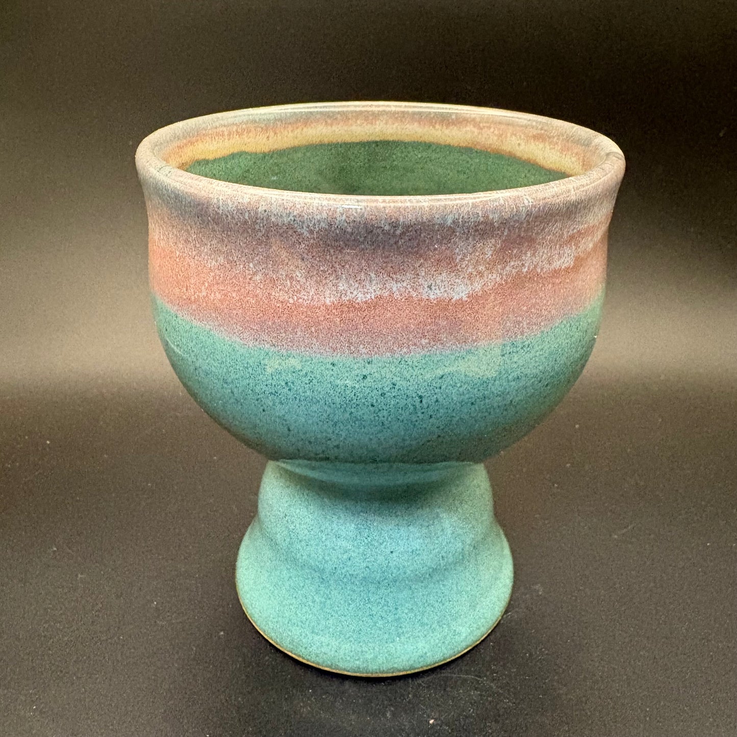 Green ceramic pedestal bowl with pink rim on grey background
